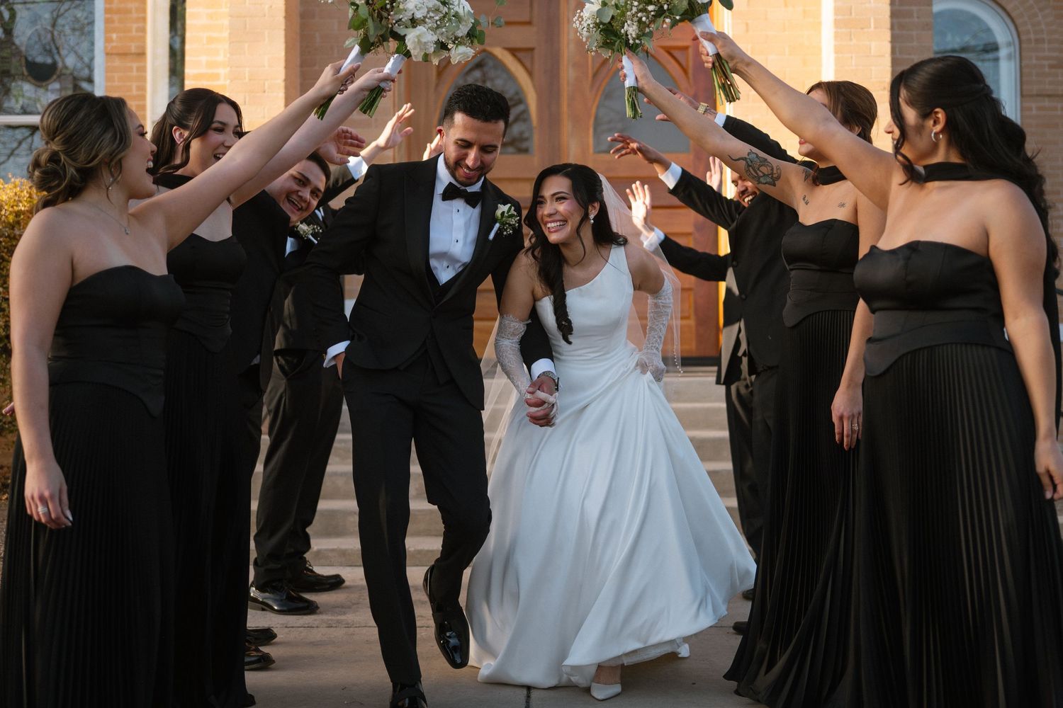 Smiling newlyweds exit church through an arch of raised hands formed by wedding party in black attire.

Corpus Christi Wedding Photographer