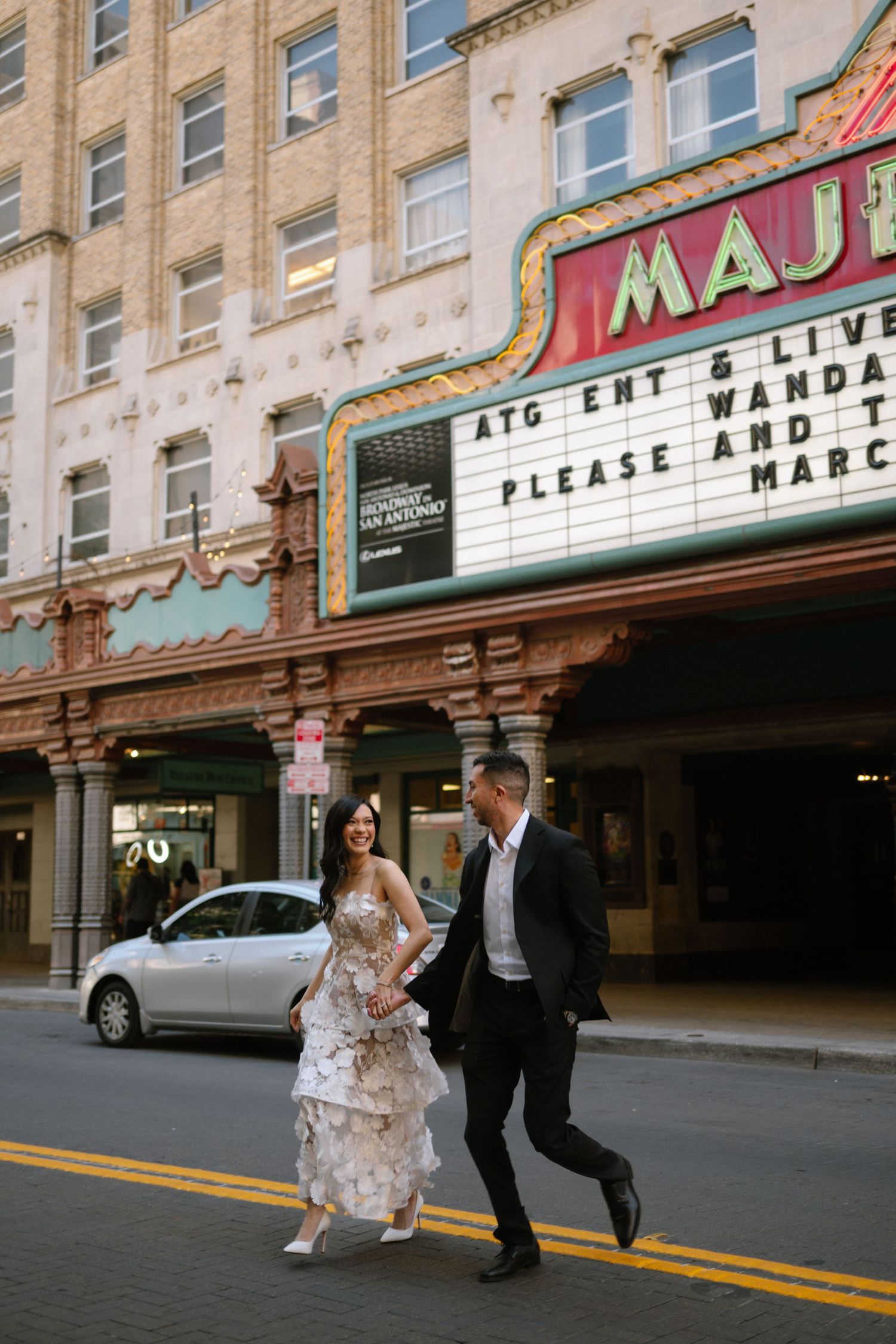 Bride and groom crossing street in front of Majestic Theatre in San Antonio, bride wearing tiered floral gown. Corpus Christi Wedding Photog