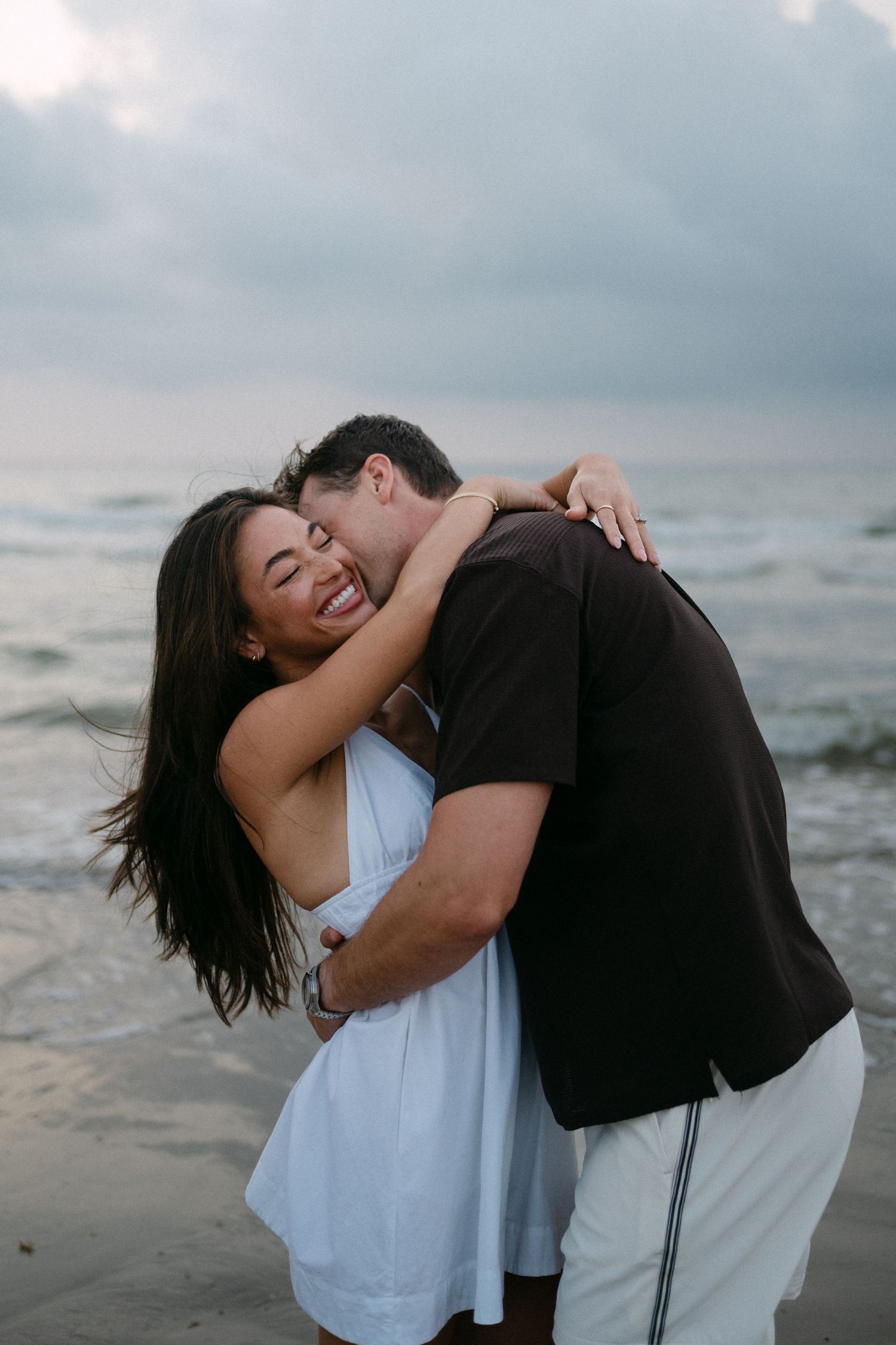 Joyful couple embracing and laughing together on a beach with ocean waves in the background. Corpus Christi Wedding Photographer