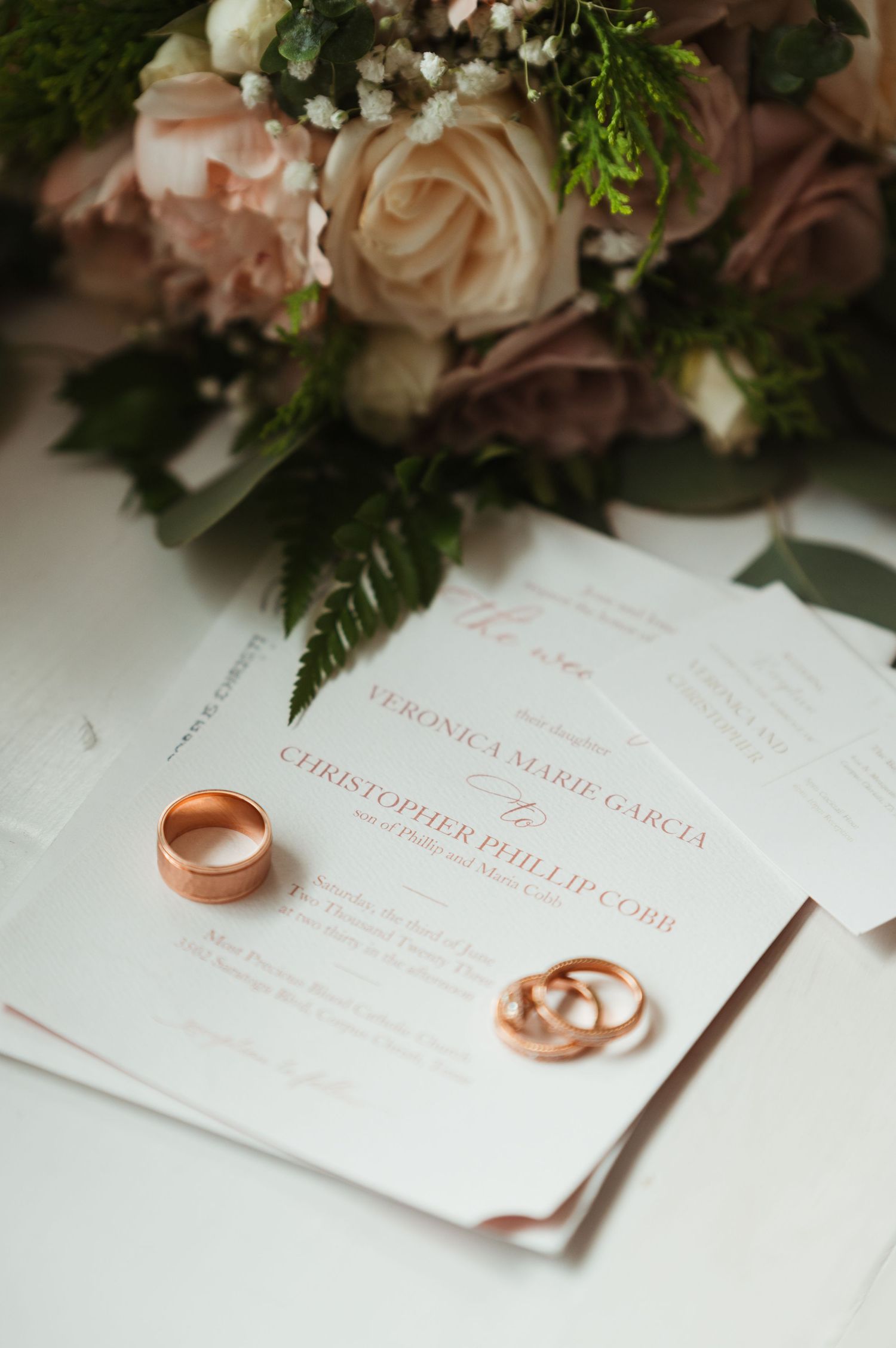 Gold wedding rings resting on wedding invitation for Veronica Marie Garcia and Christopher Phillips. Corpus Christi Wedding Photographer