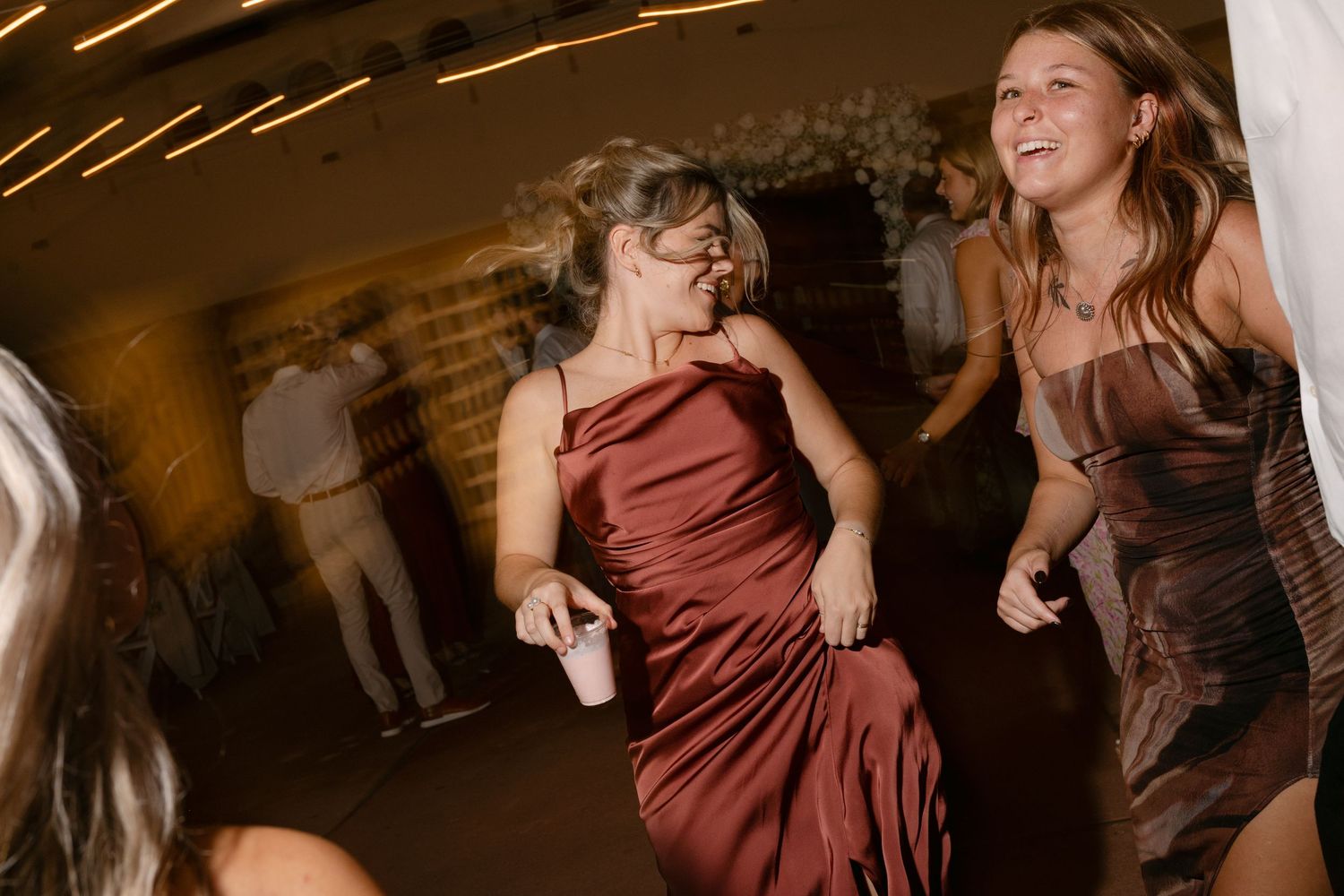 Bridesmaids in burgundy and brown dresses dancing joyfully at a lively wedding reception. Corpus Christi Wedding Photographer