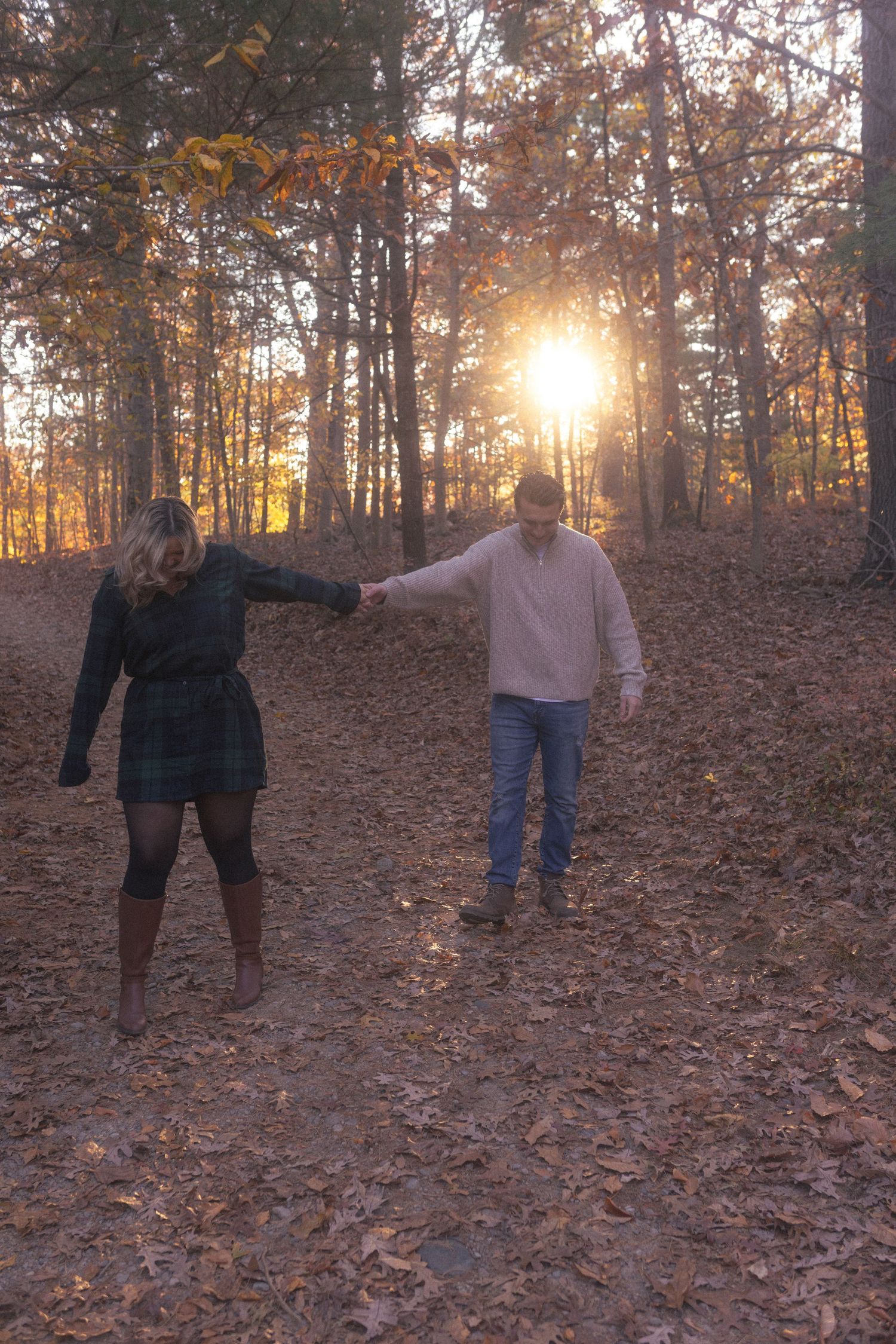 Two figures stand in a leaf-covered autumn forest during golden hour.