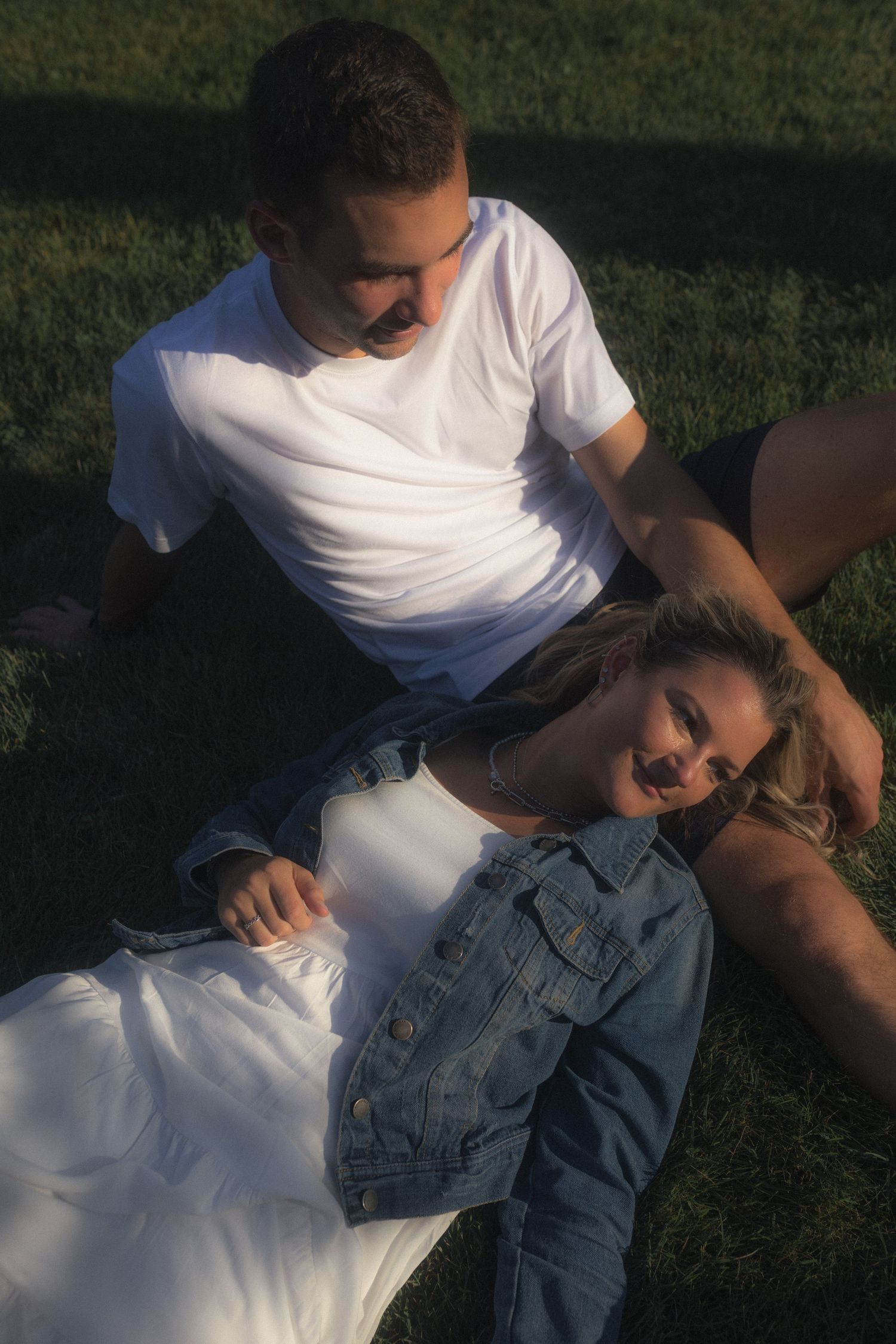 Two people share an intimate moment while relaxing on grass during golden hour.