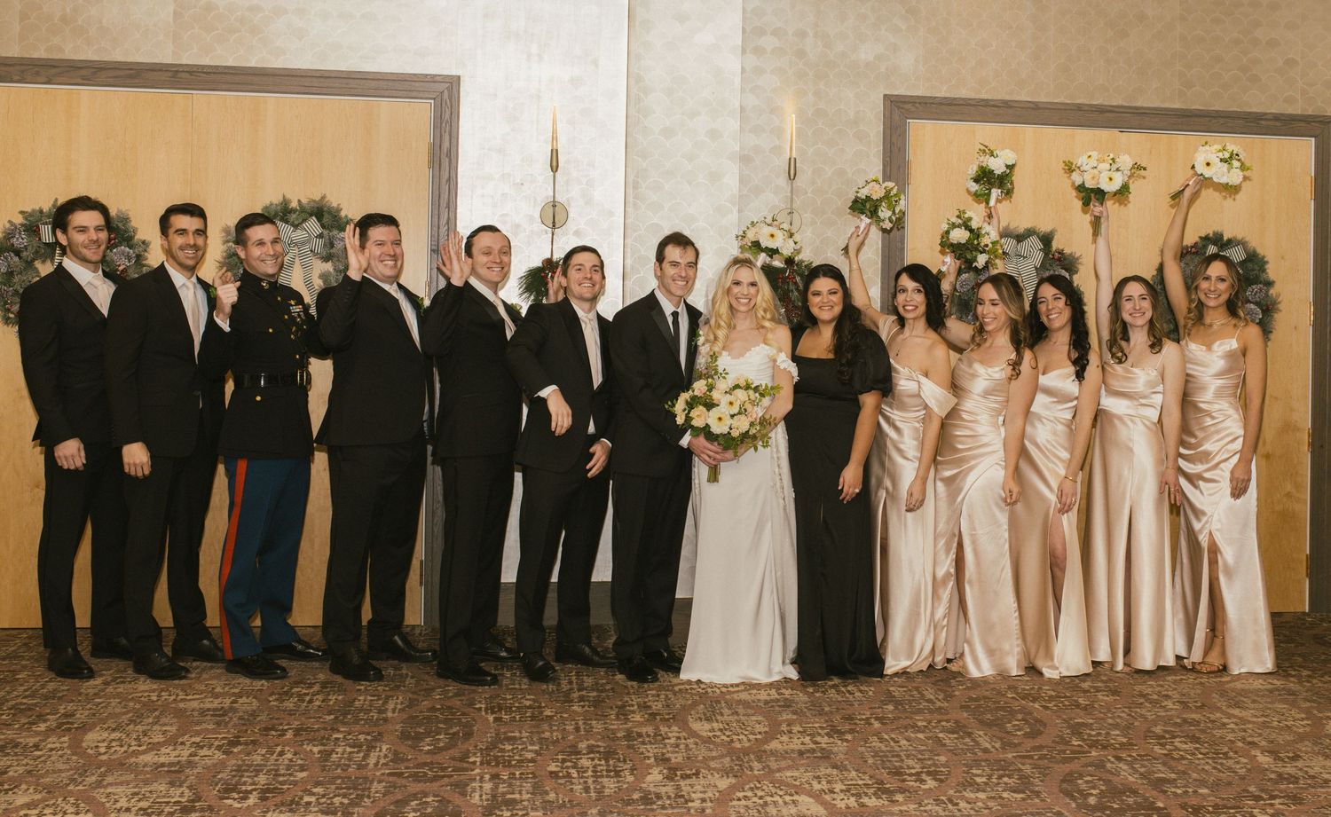 Wedding party group photo with bridesmaids in blush dresses and groomsmen in black suits.