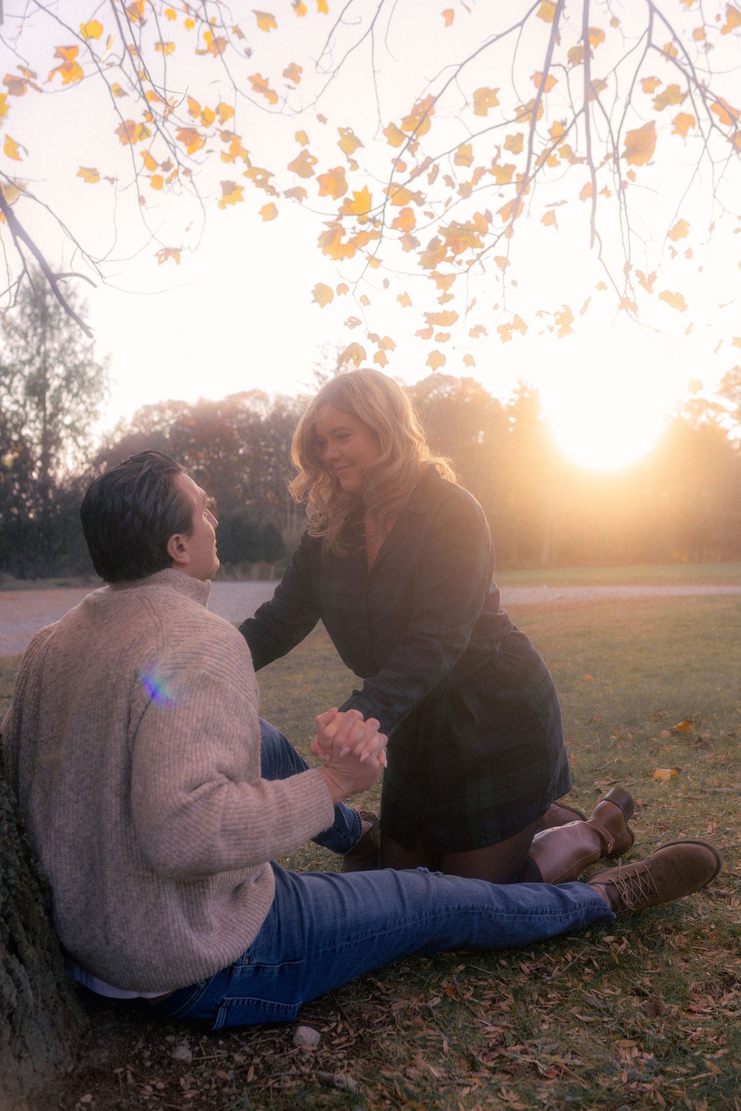 A couple sits beneath autumn trees during golden hour.