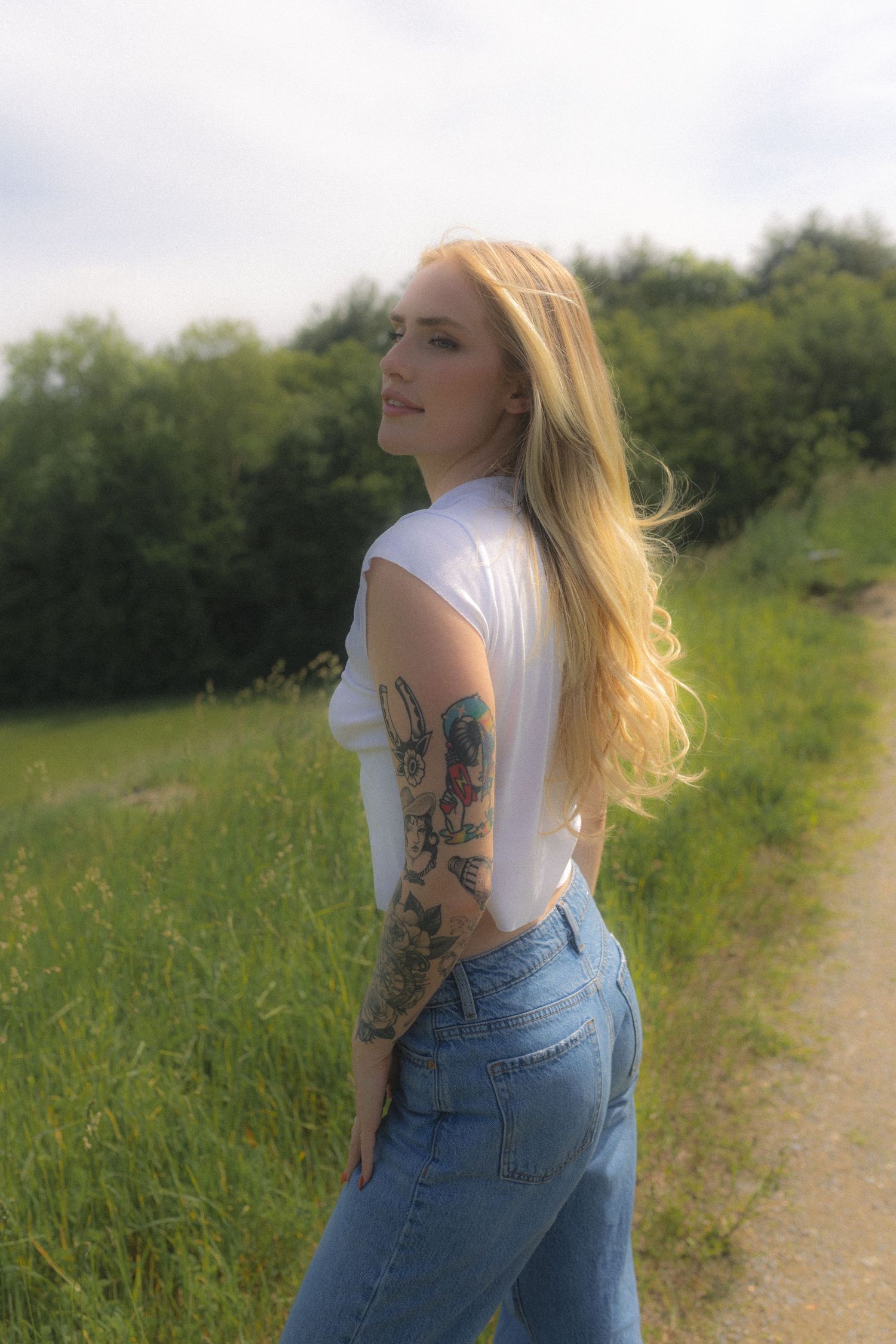 Woman in casual summer outfit poses against a scenic rural backdrop with flowing hair.