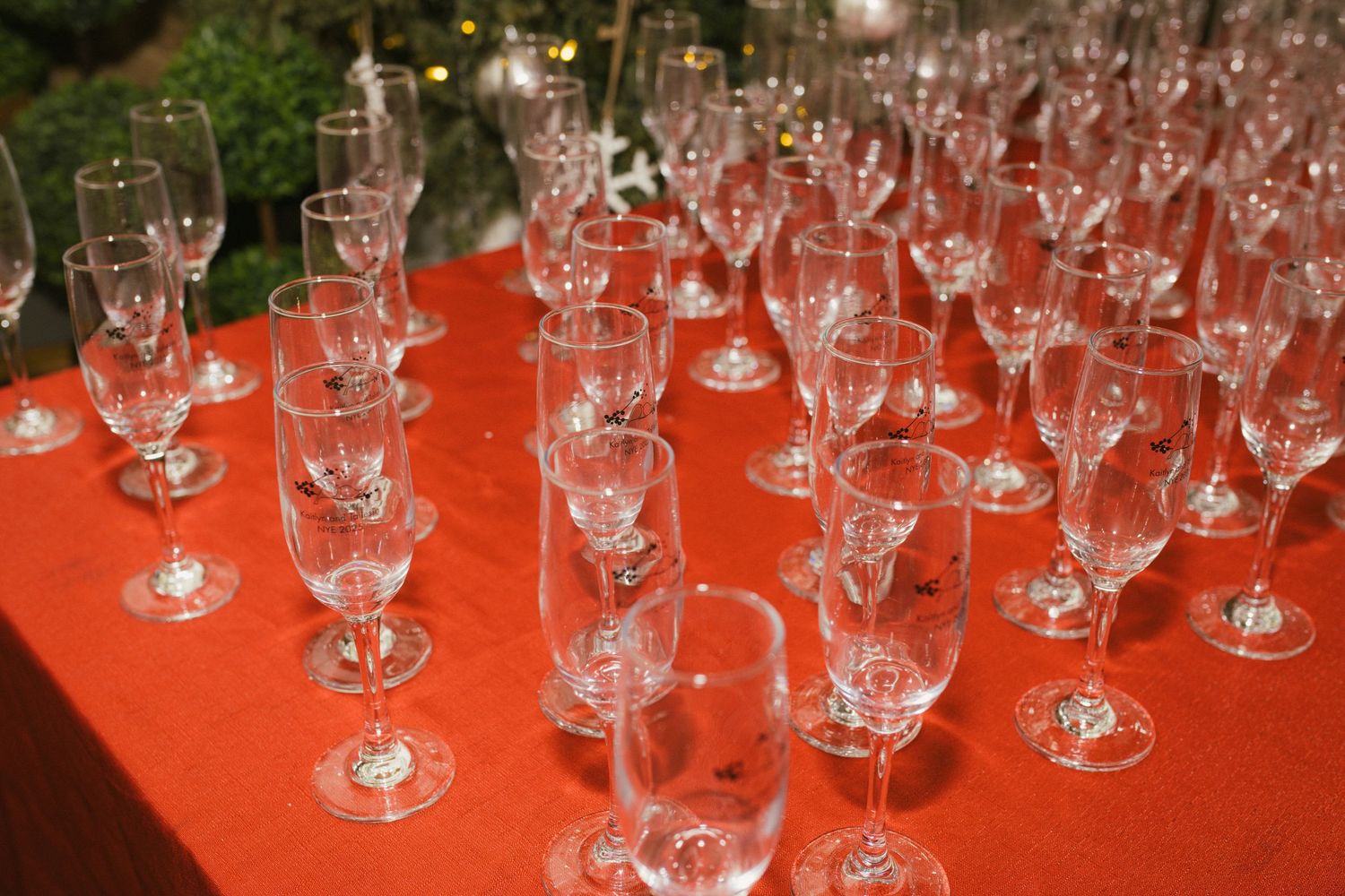 Rows of empty wine glasses arranged on a red tablecloth at a wedding reception.