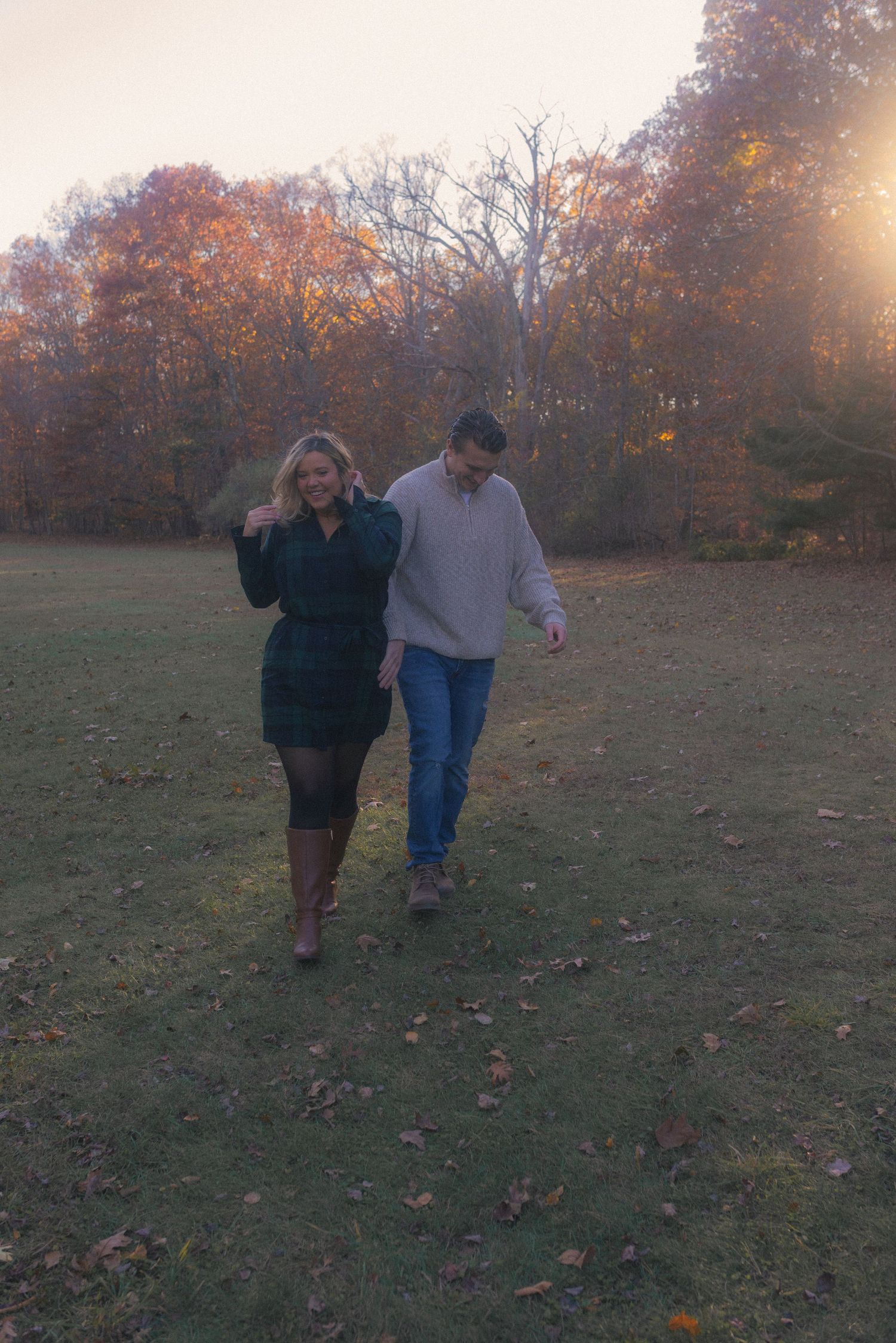 A couple strolls hand in hand across an autumn field at sunset.