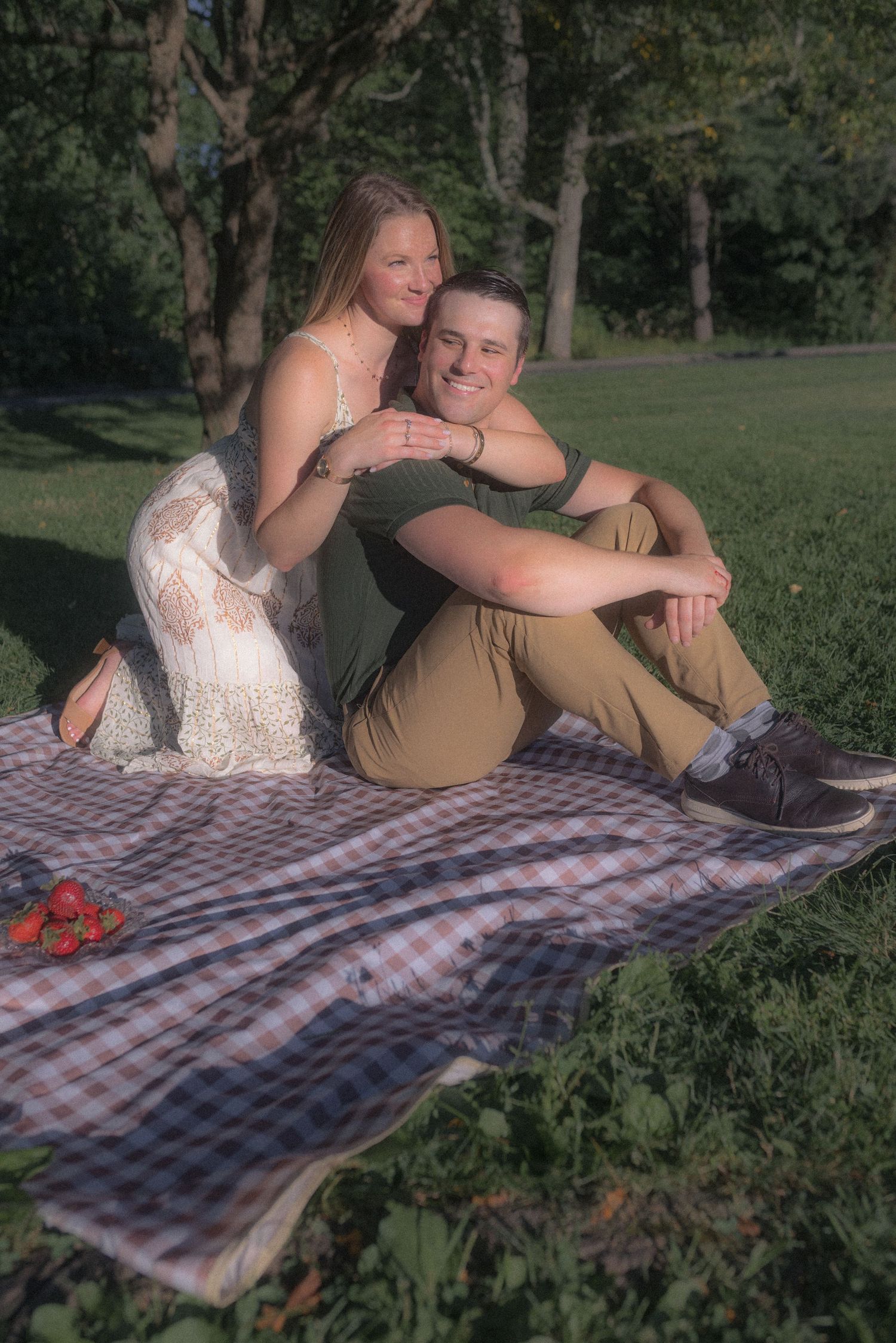 A couple relaxes together on a plaid picnic blanket in a park setting.