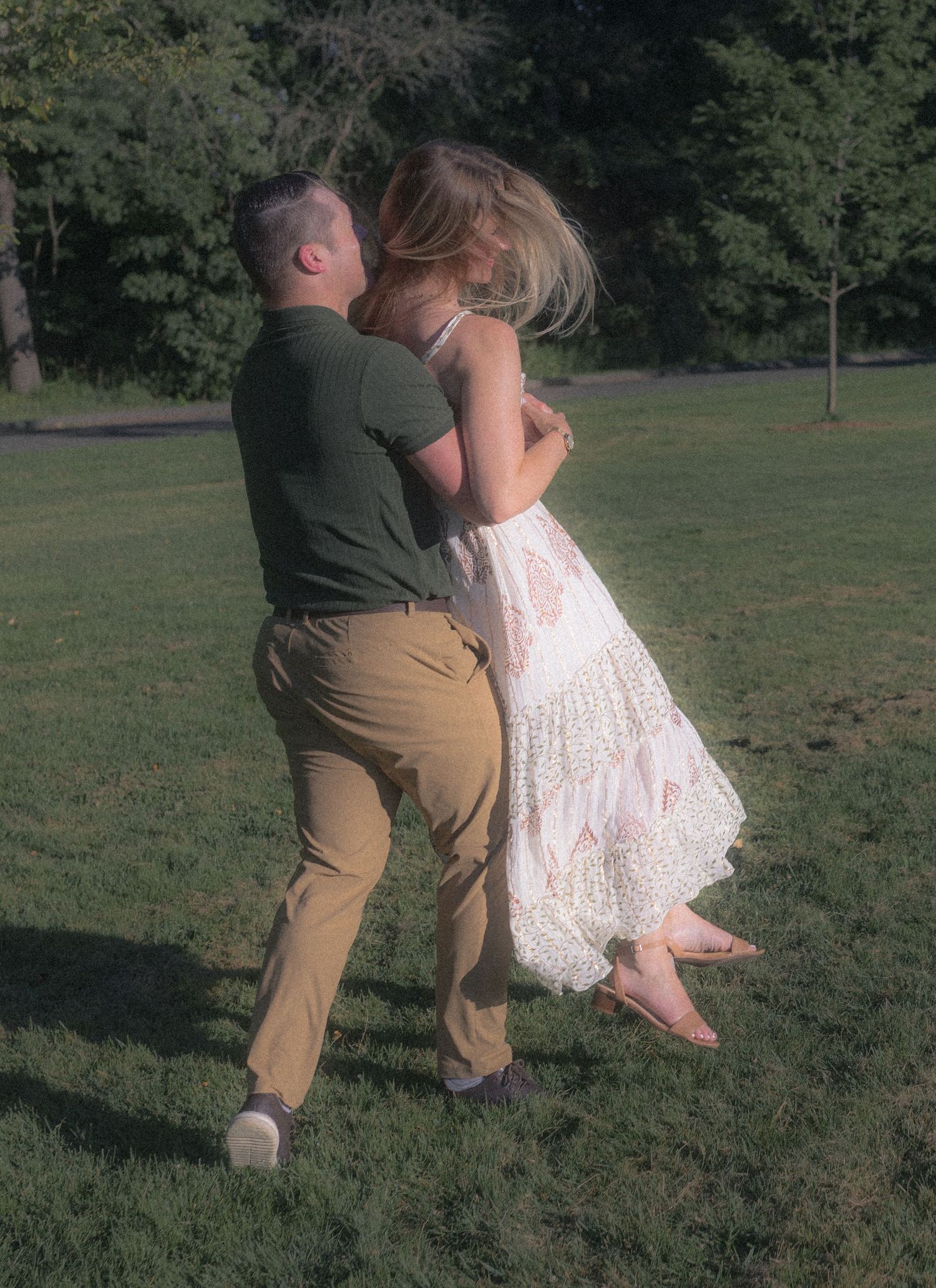 A couple embraces in a romantic moment on a grassy hill during a sunny afternoon.