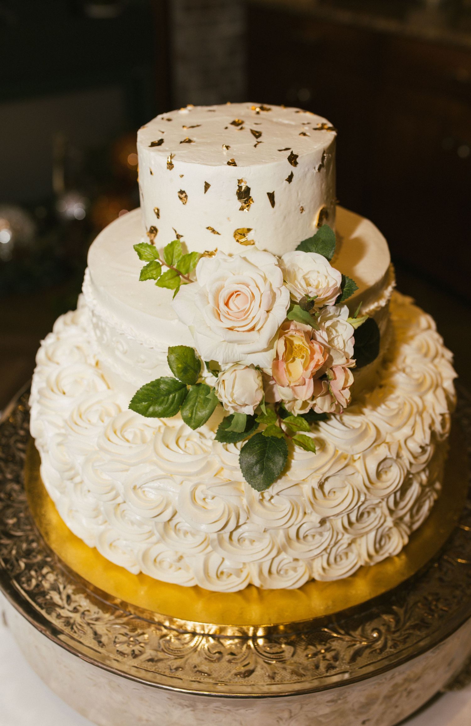 Two-tiered white wedding cake decorated with fresh roses and rosette frosting details.