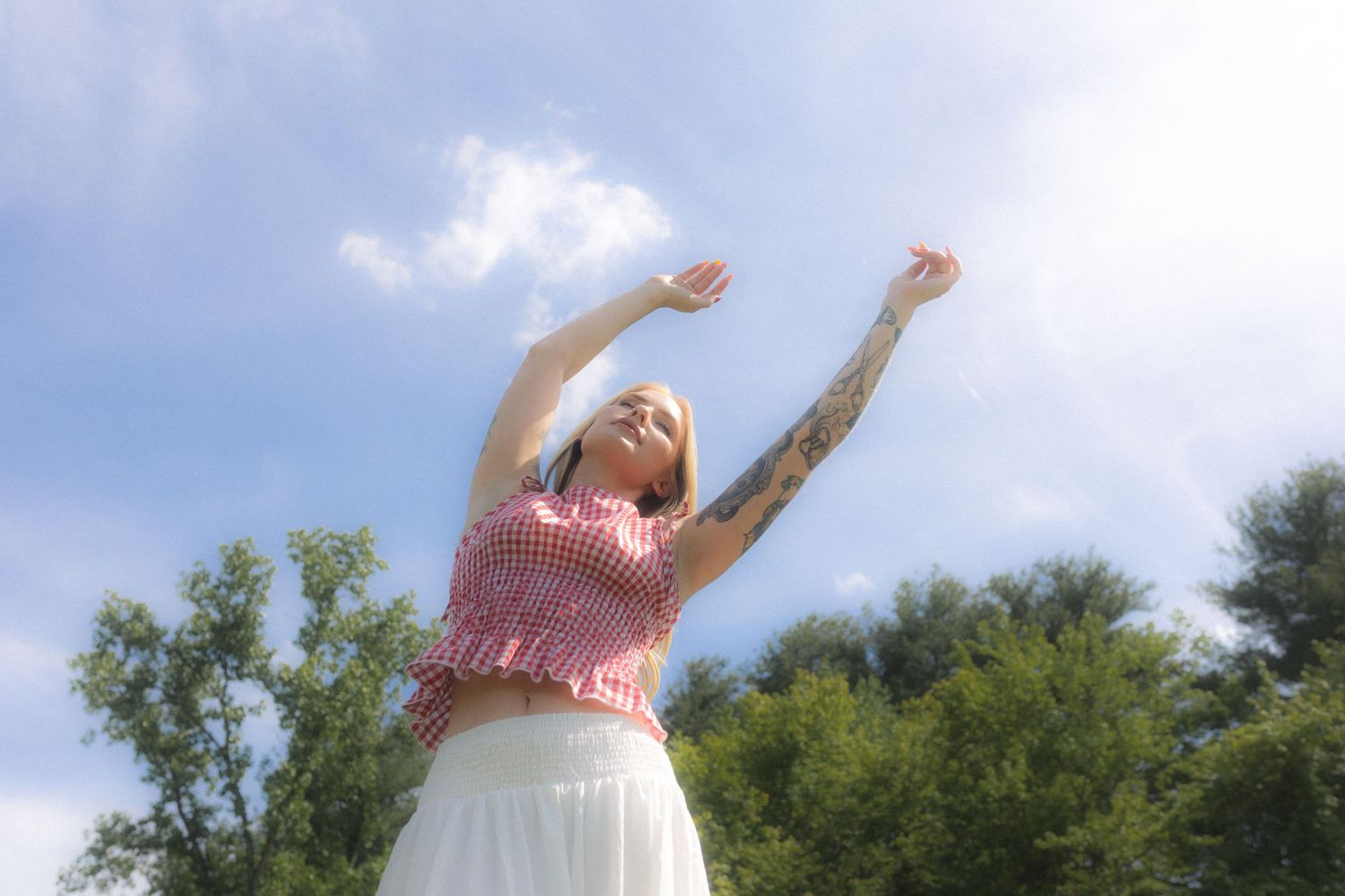 Person in pink dress twirling joyfully outdoors against blue sky.