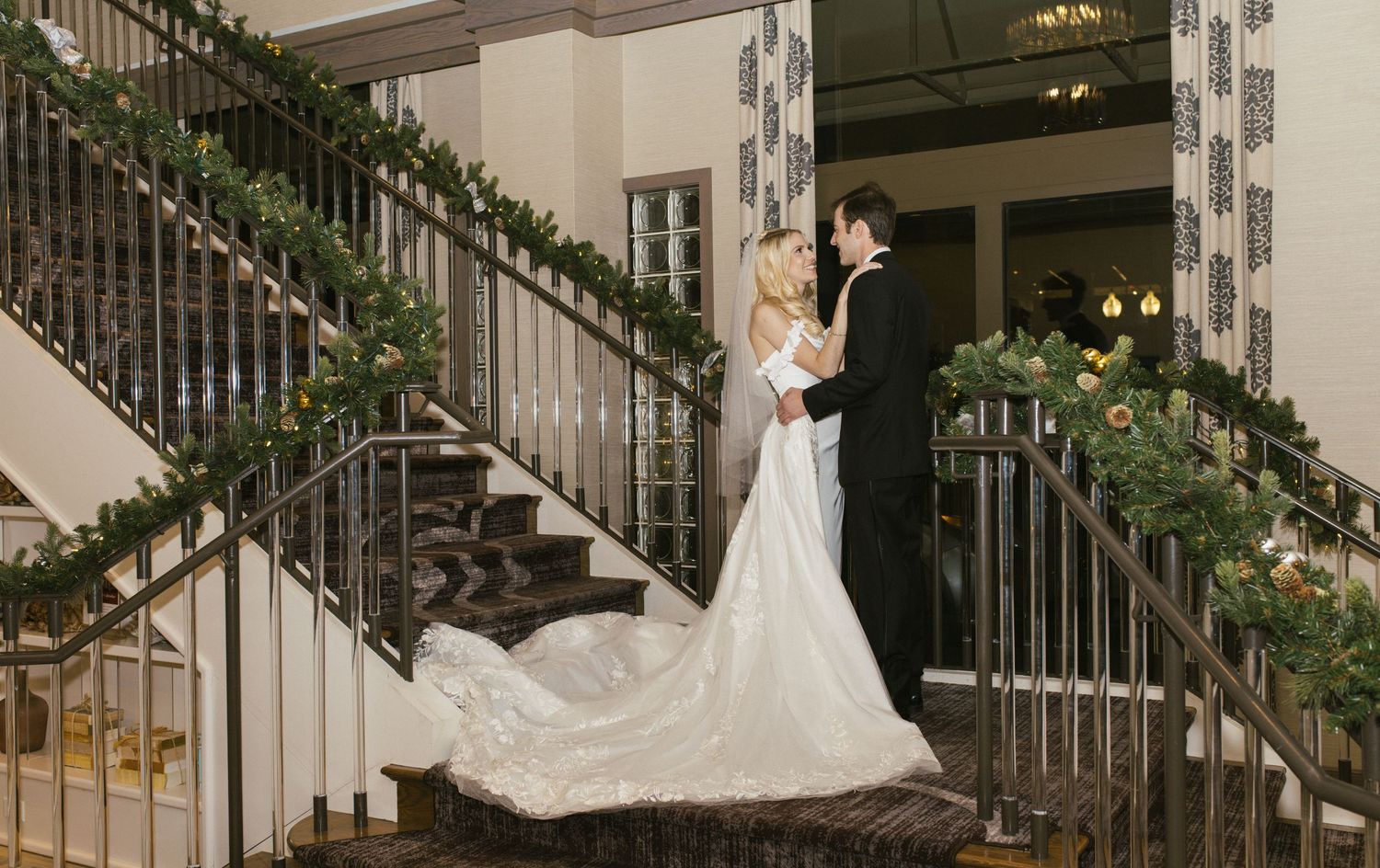 Elegant wedding scene with couple dancing on grand staircase decorated with greenery.