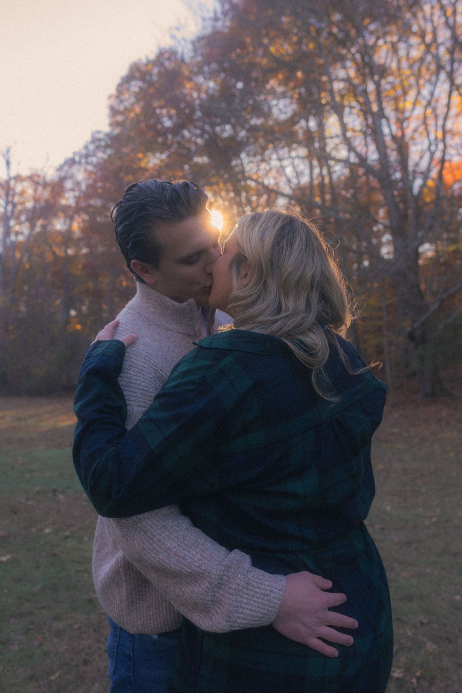 A romantic embrace captured at sunset with golden light filtering through autumn trees.