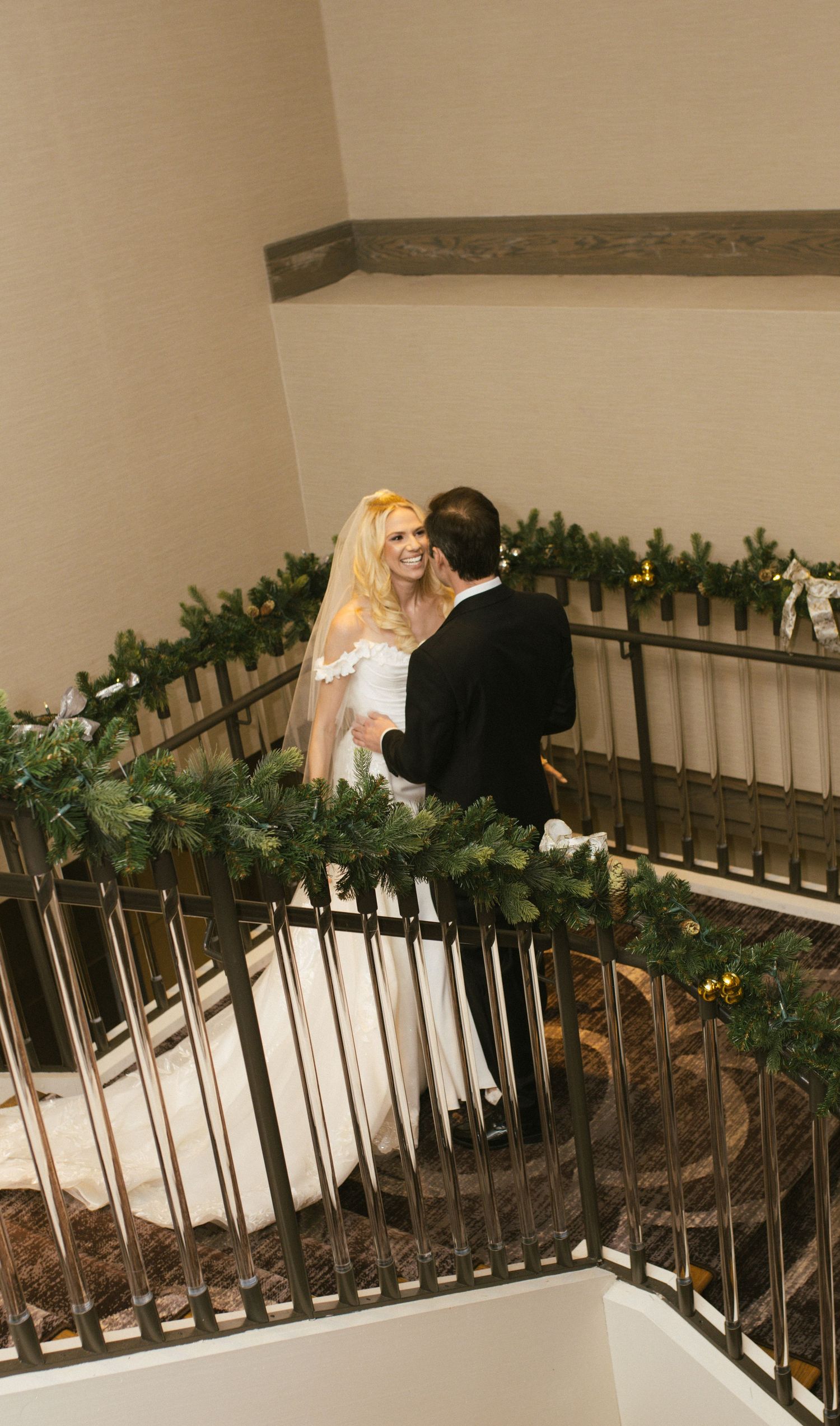 Wedding couple descending a decorated staircase with greenery and lights.