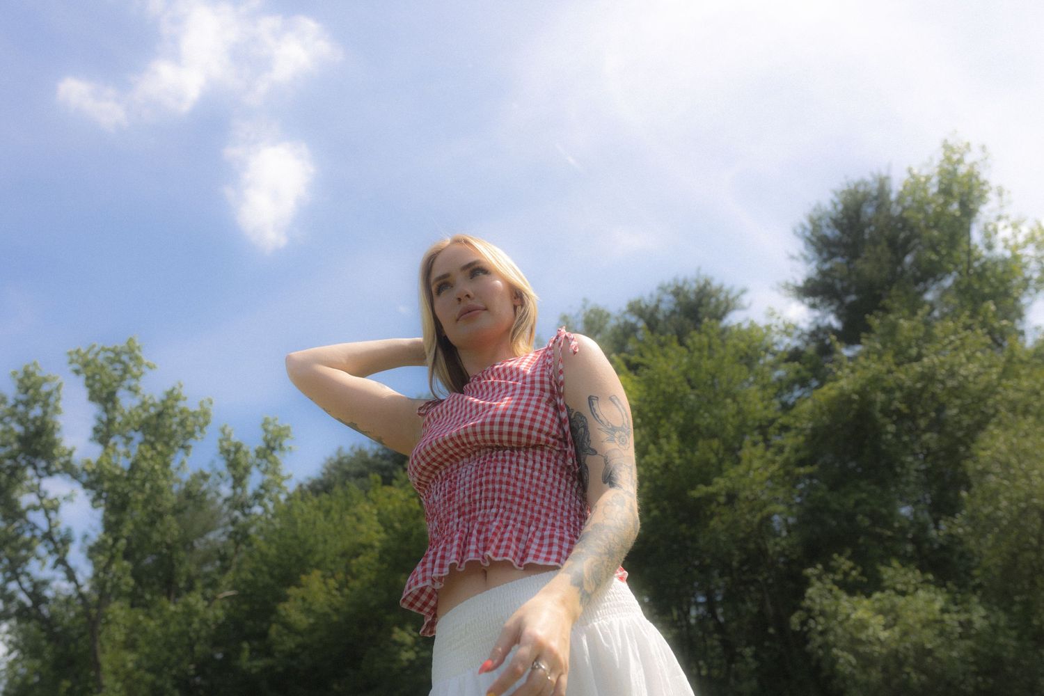 Carefree poses in a red and white gingham top with a flowing white skirt outdoors.