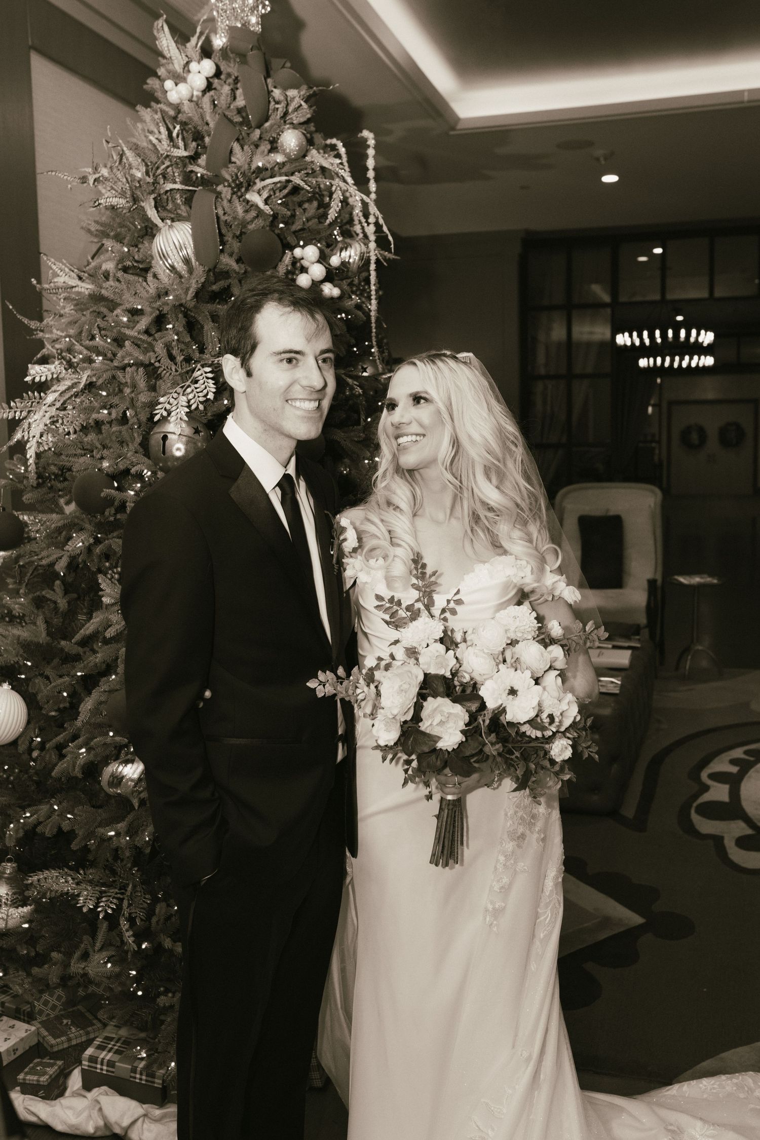 A wedding couple poses in front of a decorated Christmas tree at their winter reception.