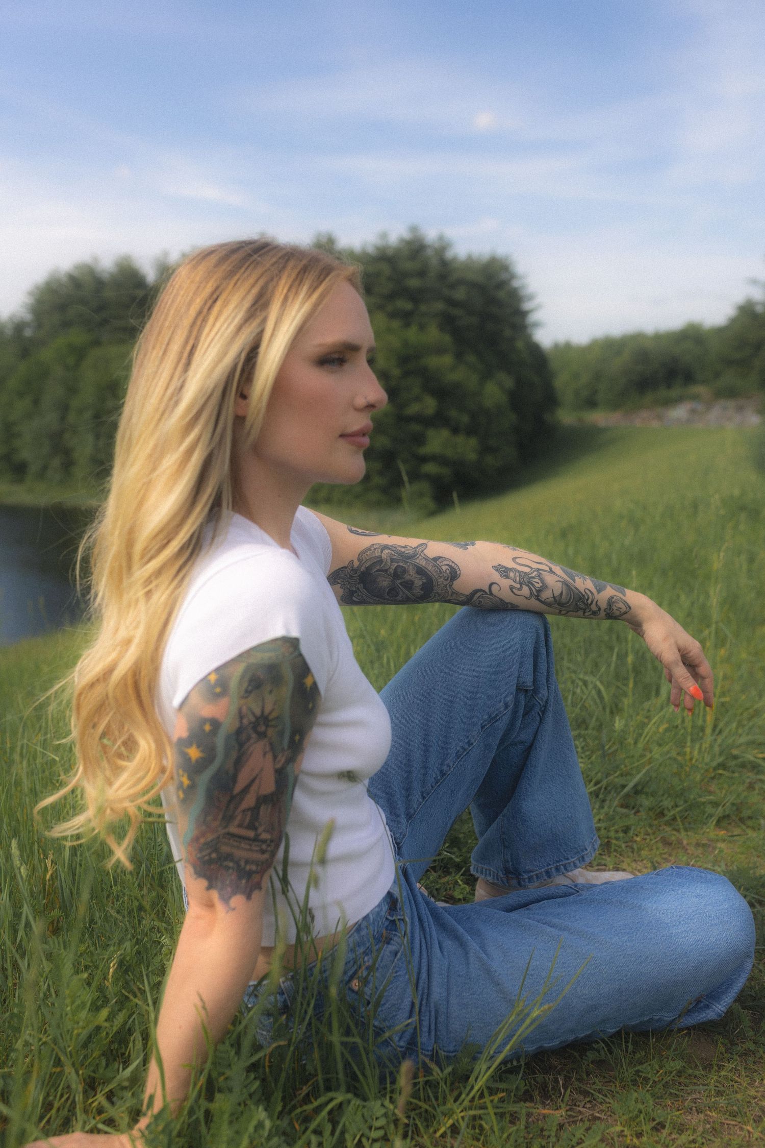 Woman in white top and jeans lounging in a grassy field on a sunny day.