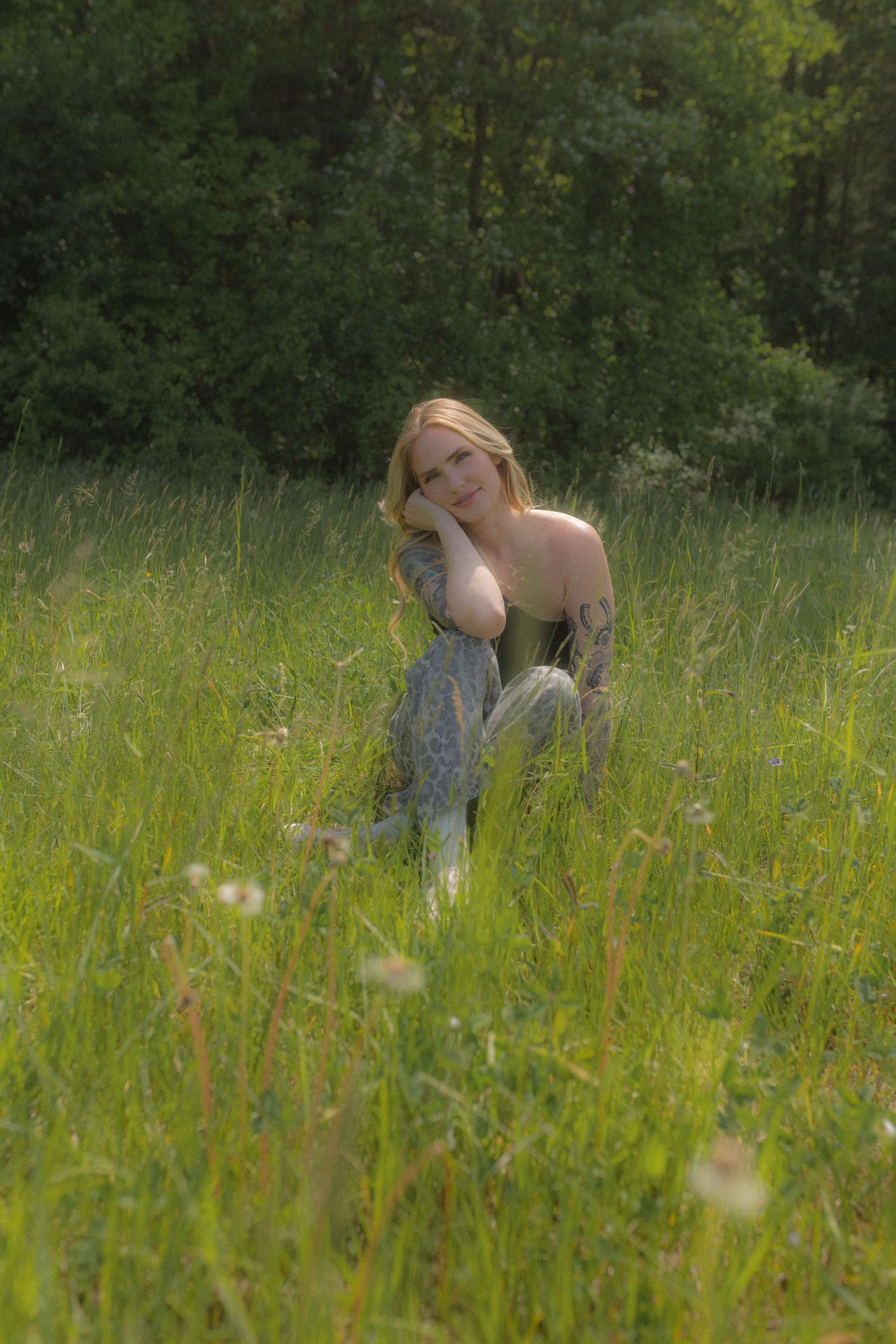 Dreamy photoshoot in a tall grass meadow with natural sunlight filtering through trees.