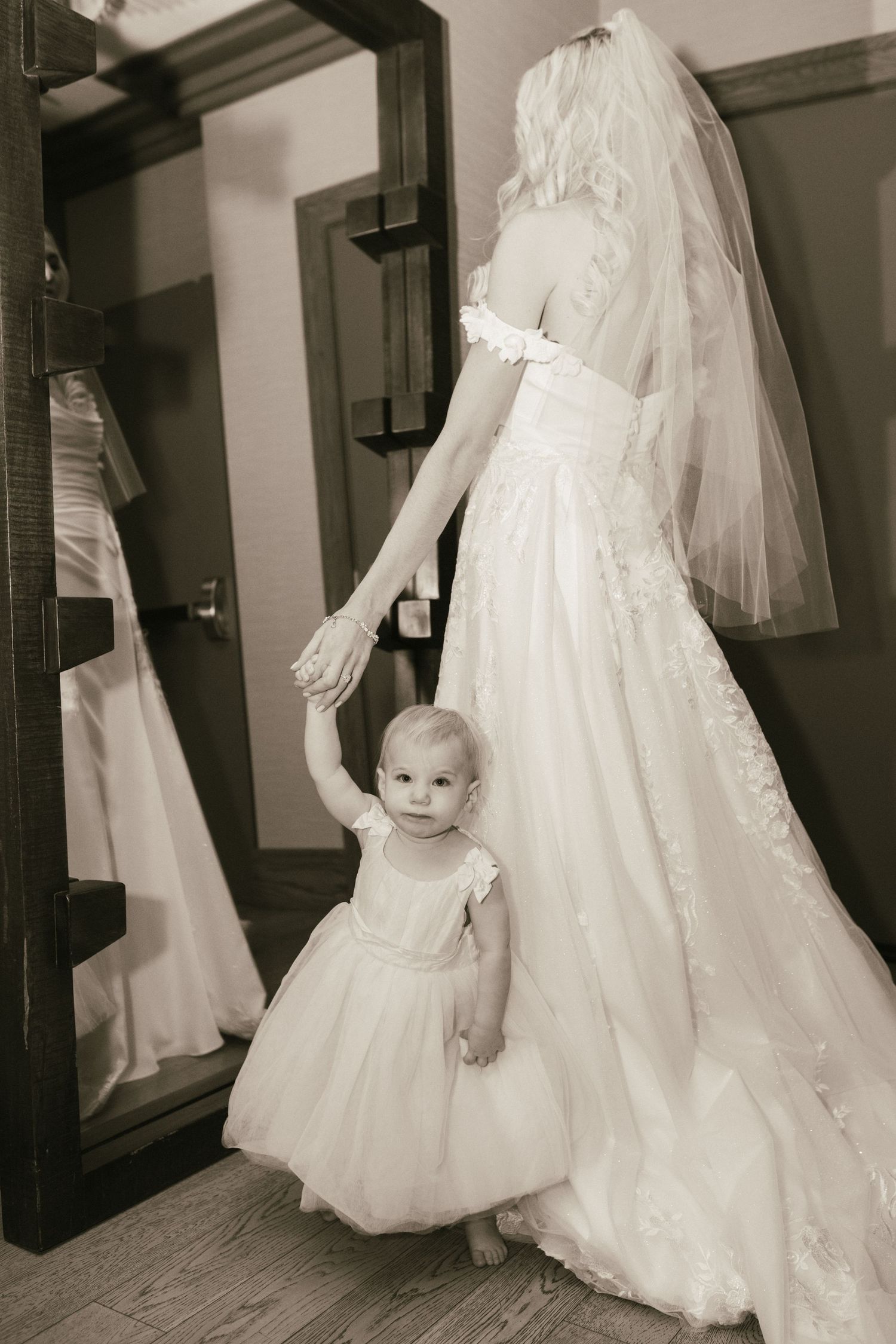 Black and white image of wedding dress preparations in a hallway with mirrors.