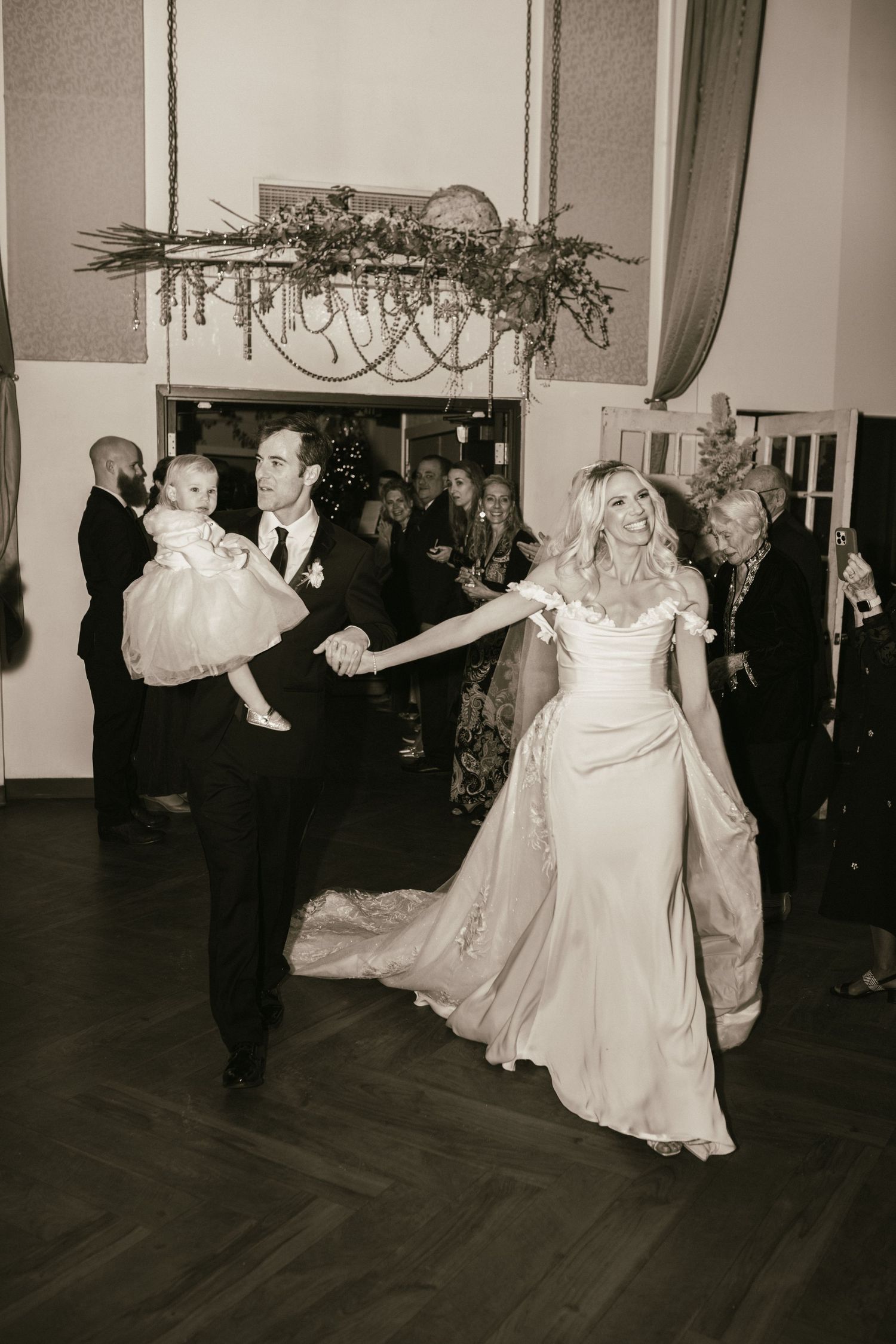 Wedding guests dancing and celebrating on a dark wooden dance floor at an elegant reception venue.