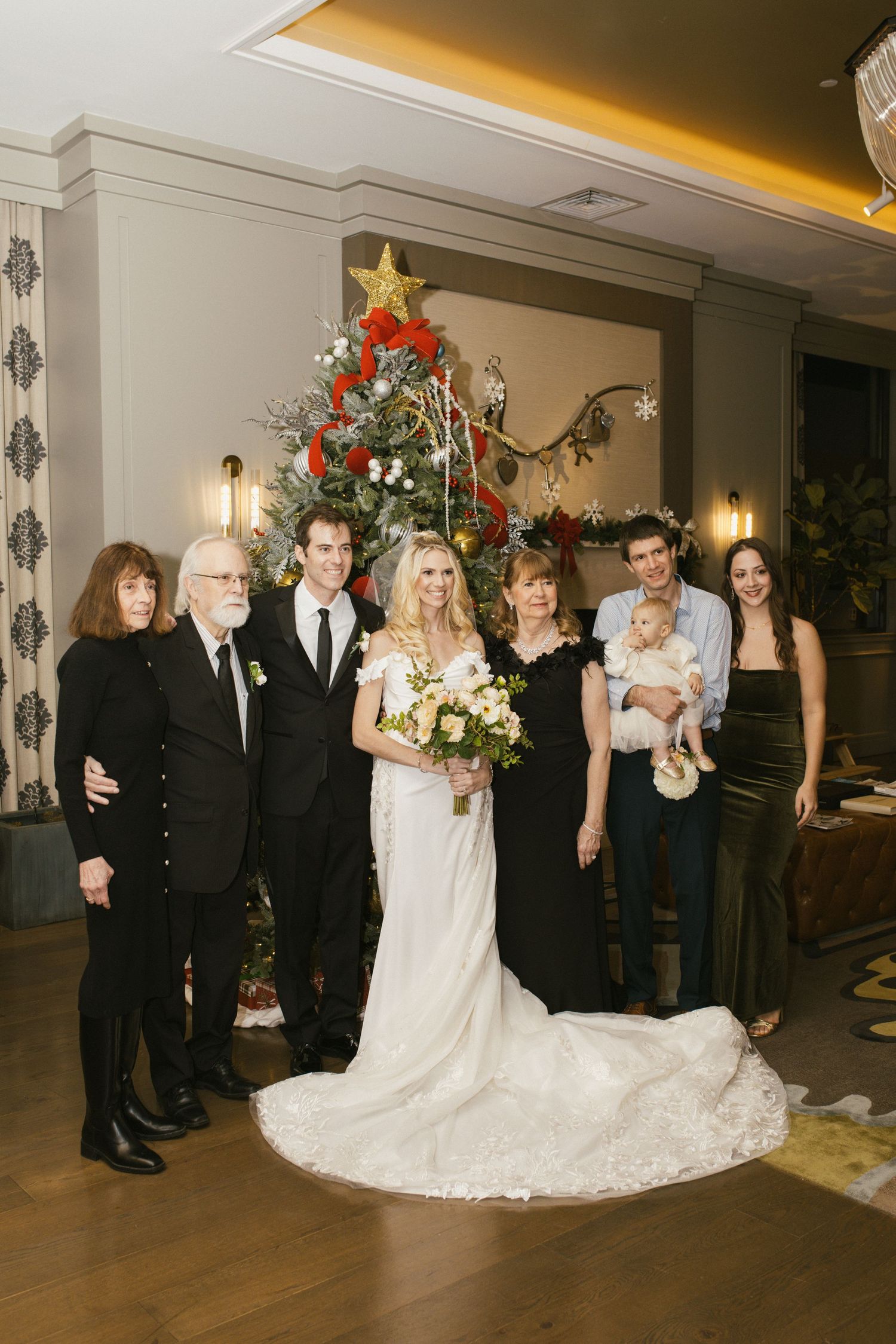 A wedding party group photo with a Christmas tree and elegant decor.
