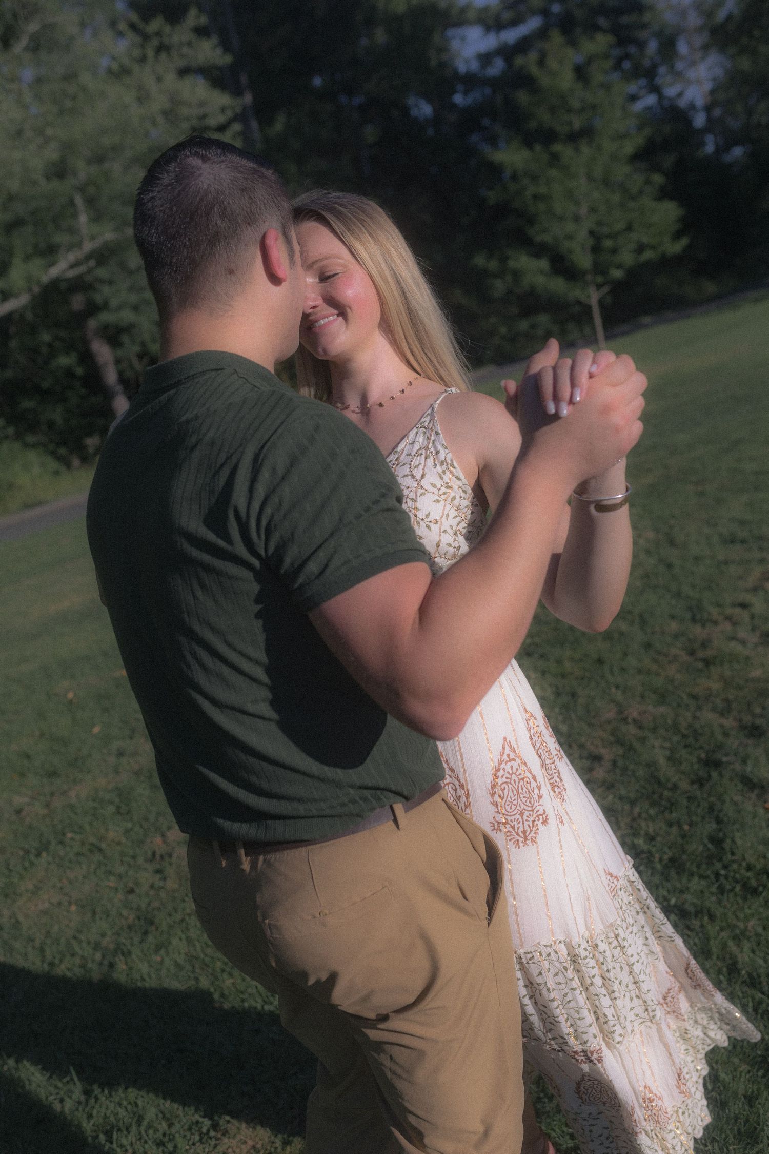 A couple shares an intimate dance in a park setting with natural lighting.