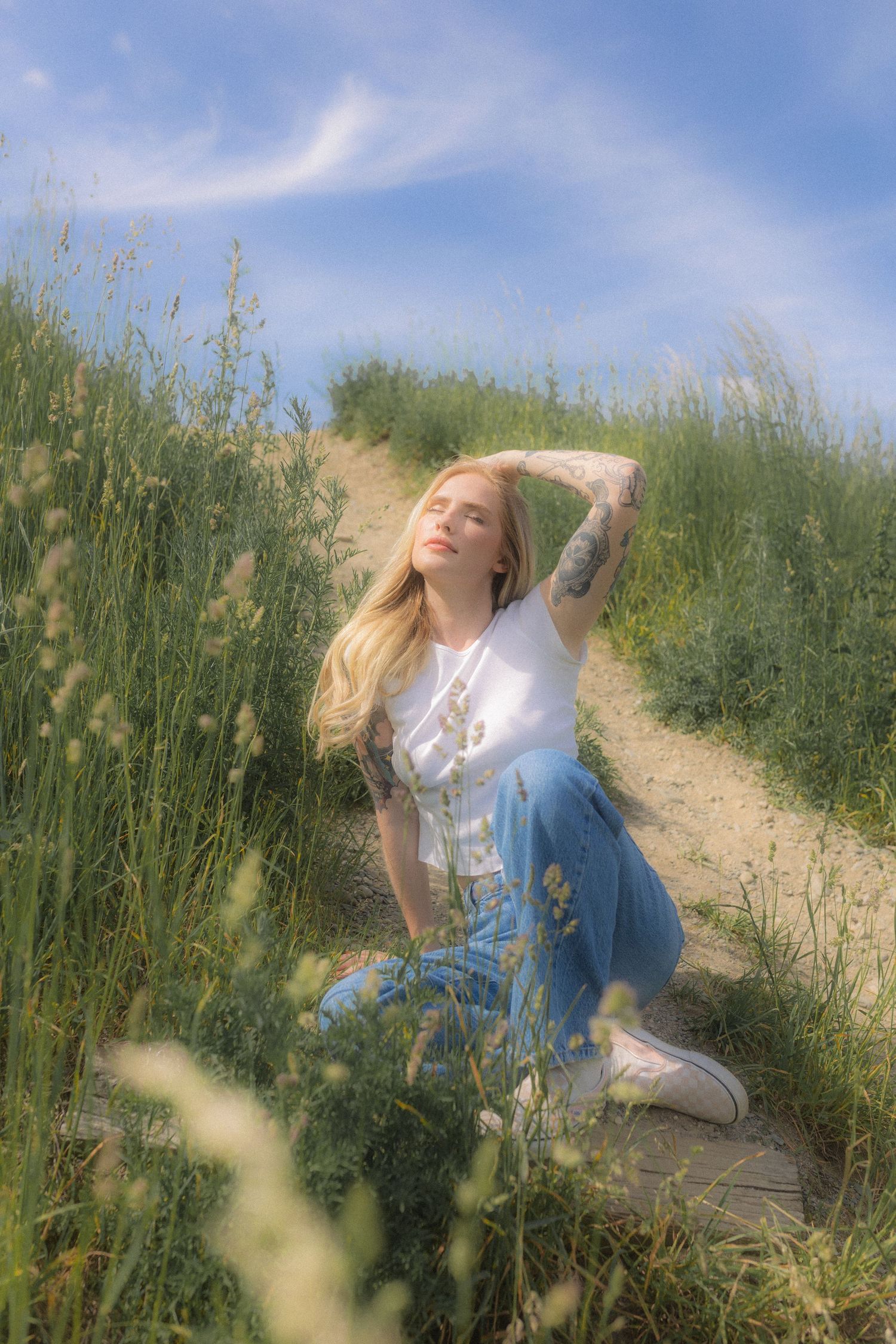 Artistic poses among tall grasses on a winding dirt path under blue skies.