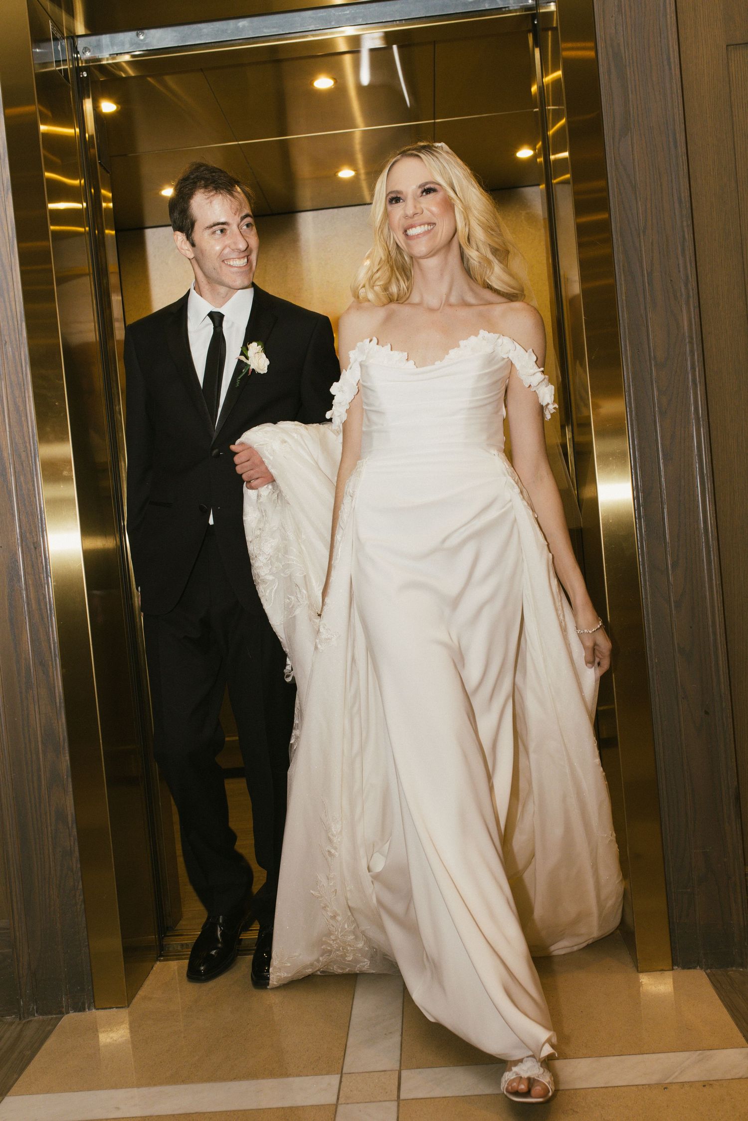 Couple exits elevator together in elegant wedding attire.