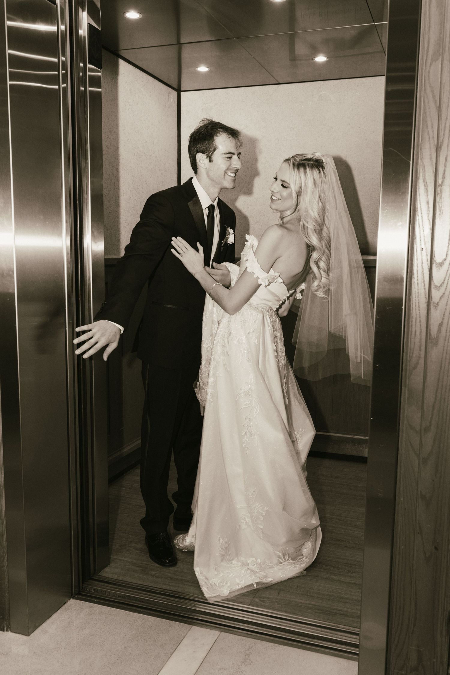 Wedding couple embracing in an elegant elevator with reflective surfaces.
