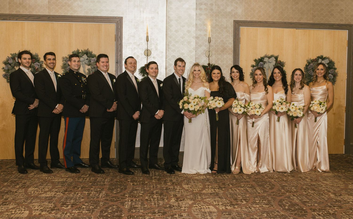 Wedding party lined up in formal attire against neutral background.