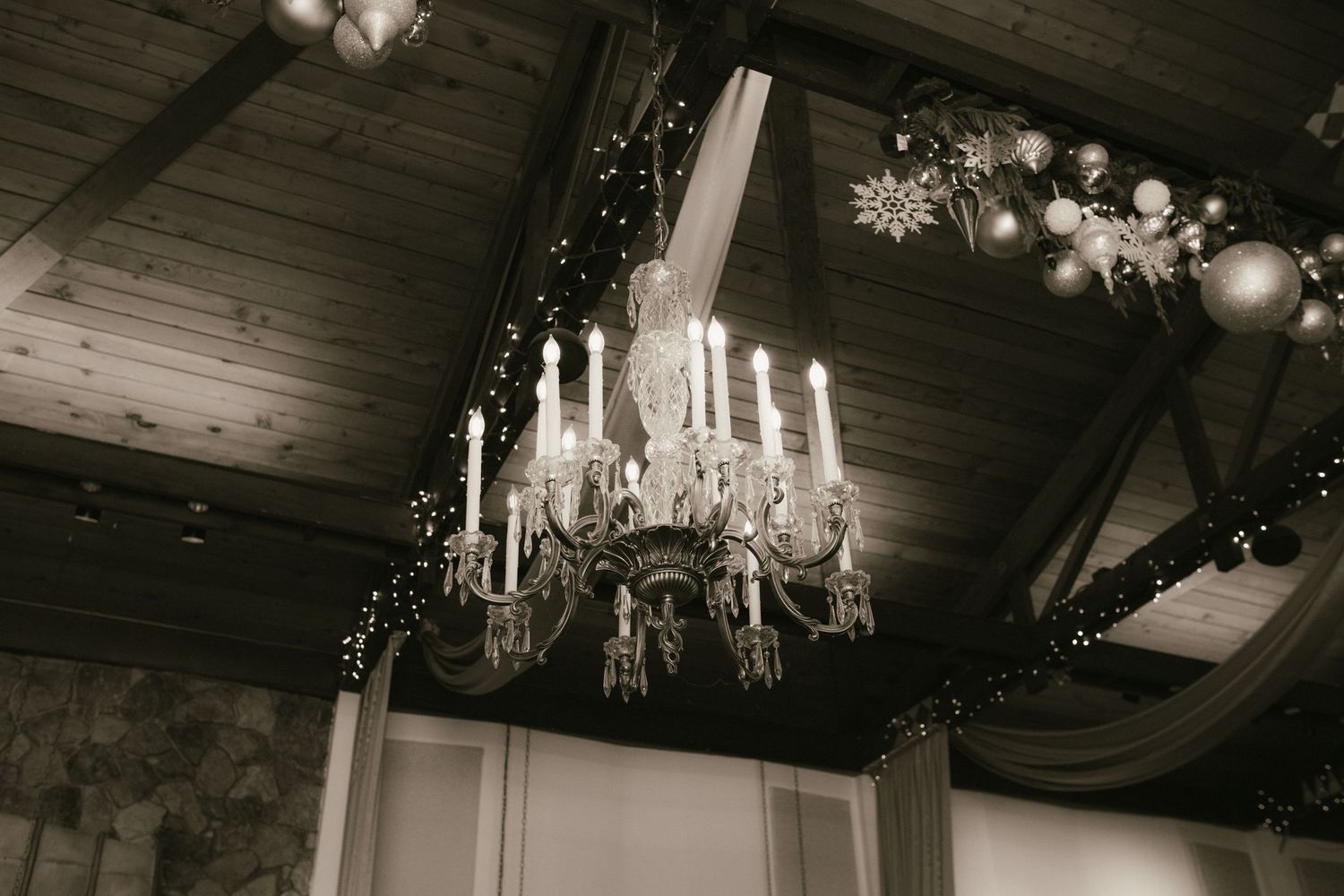 Vintage crystal chandeliers hanging from dark wooden beams in event space.