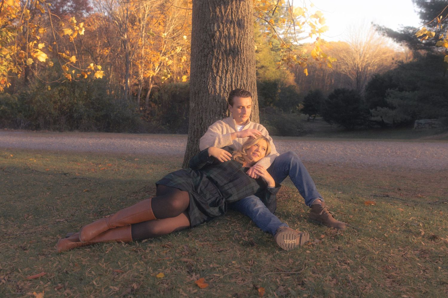 A couple rests together on fallen leaves in an autumn forest setting.