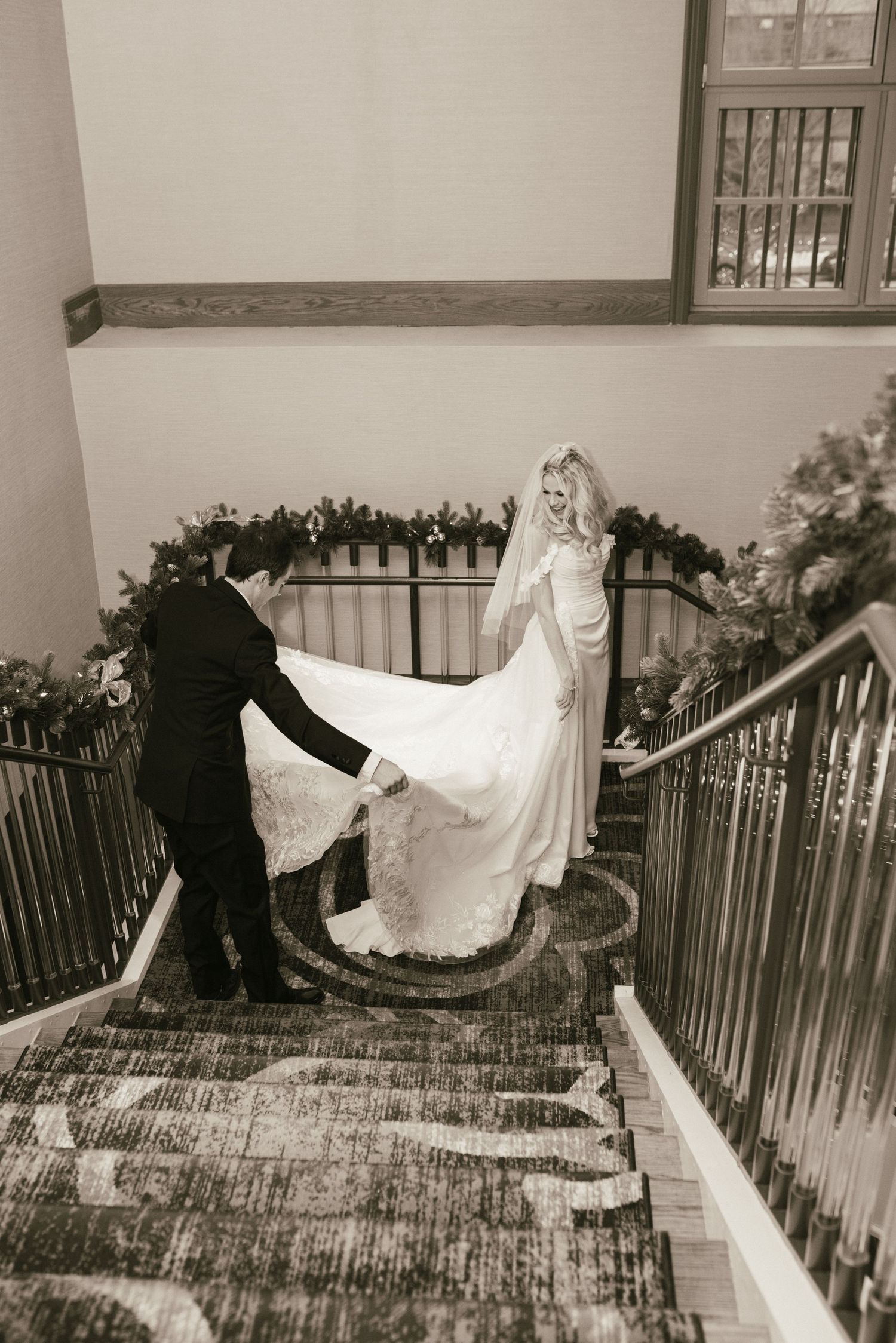 Black and white photo of newlyweds on ornate staircase during wedding celebration.