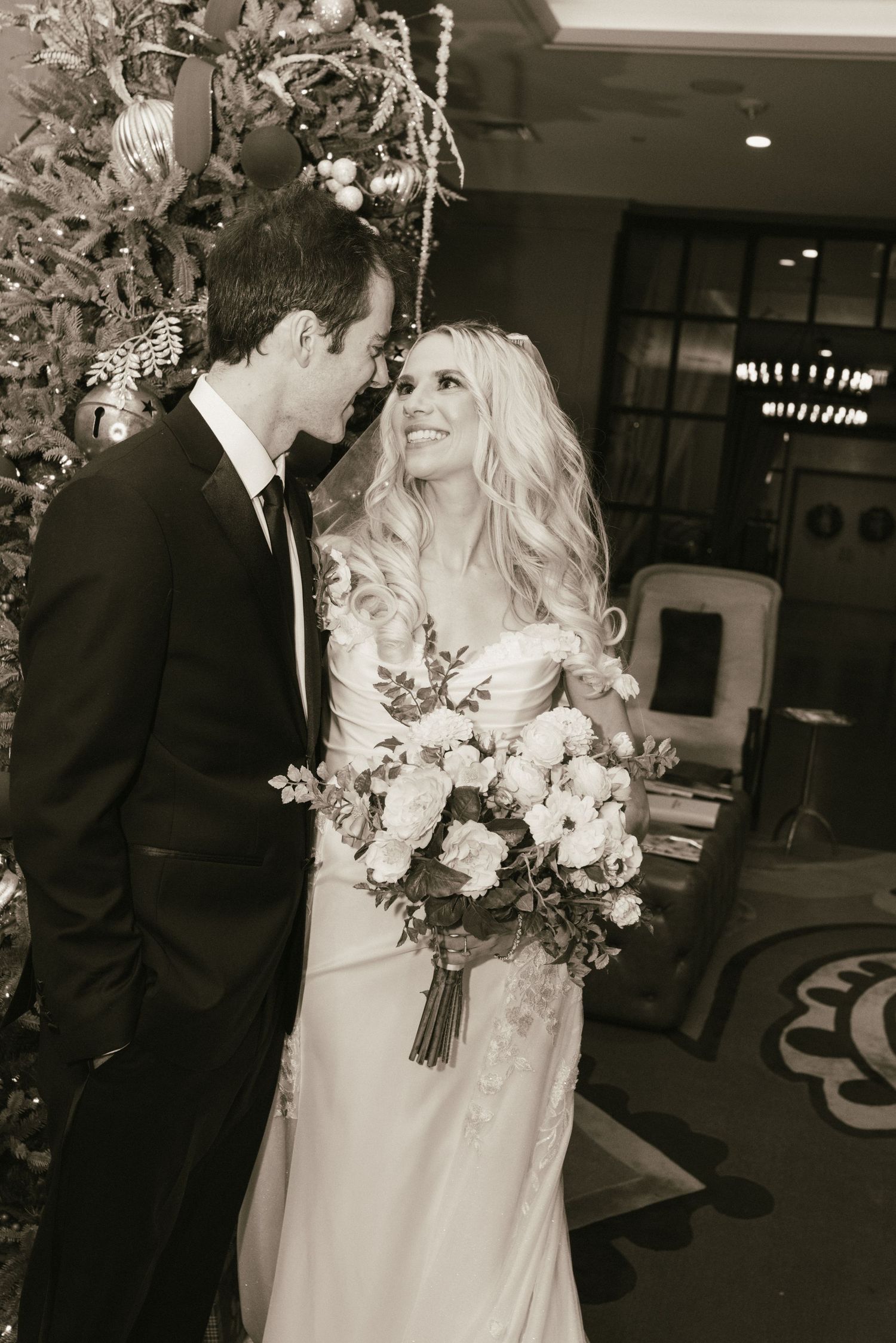 Romantic black and white moment between couple by decorated Christmas tree with elegant bouquet.