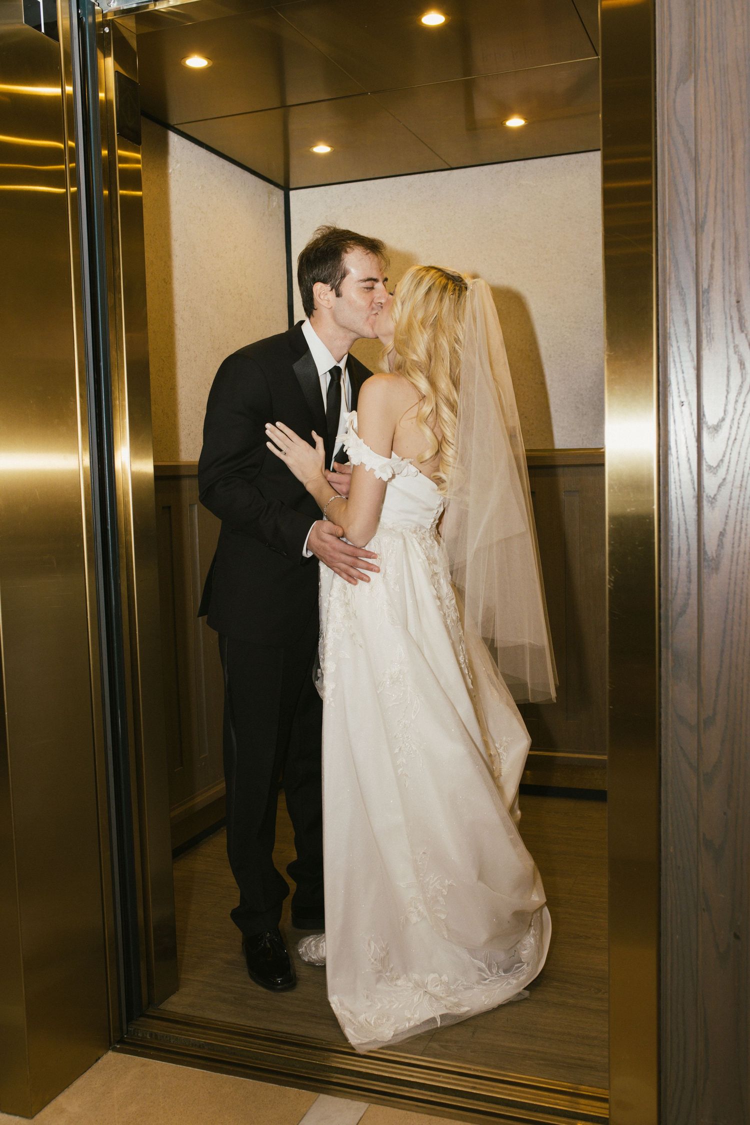 Romantic elevator moment between newlyweds in formal wedding attire.