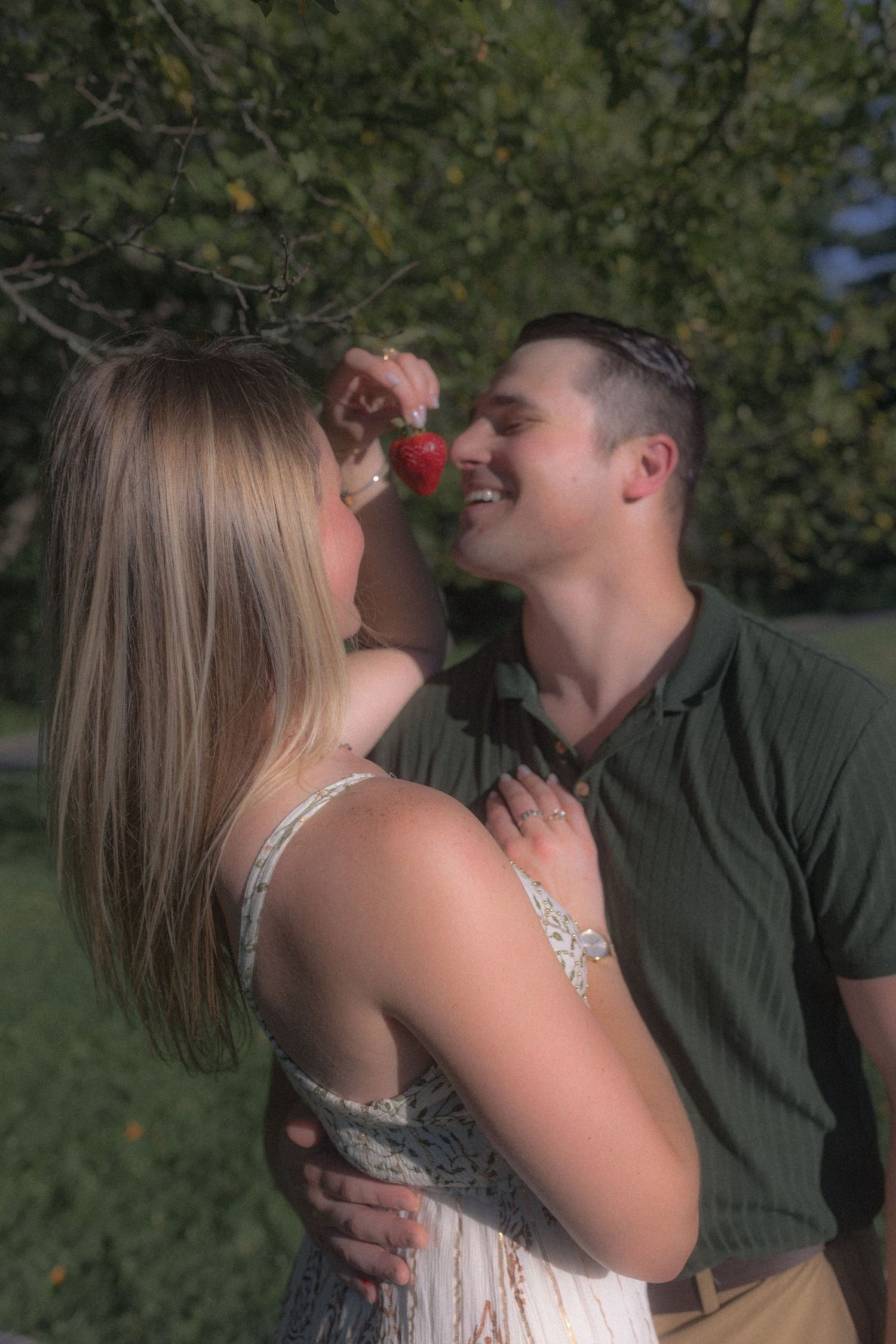 A tender moment between a couple outdoors with trees in the background.