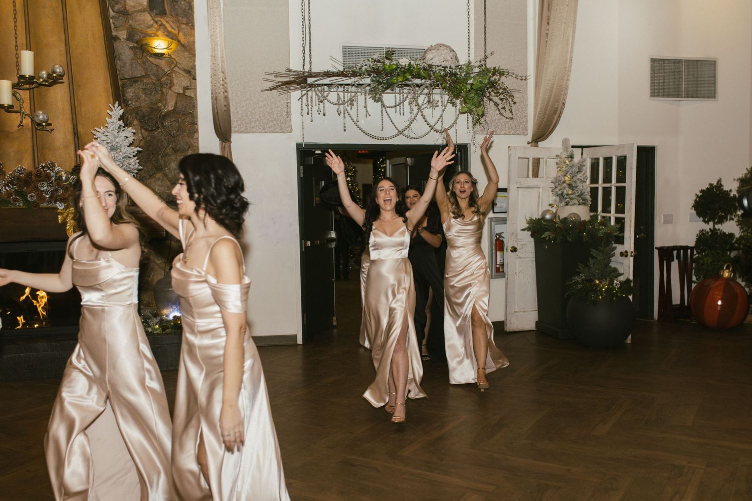 Wedding party members in champagne-colored dresses dancing on a wooden dance floor.