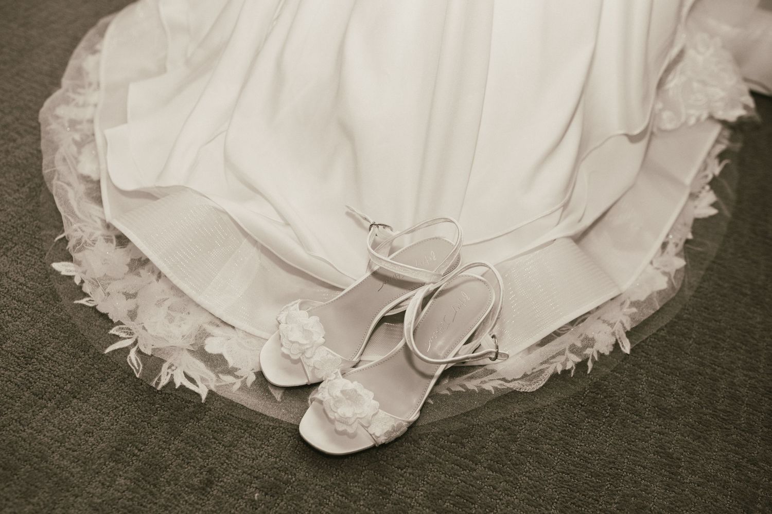 Close-up details of a white wedding dress train with delicate lace trim on carpet.