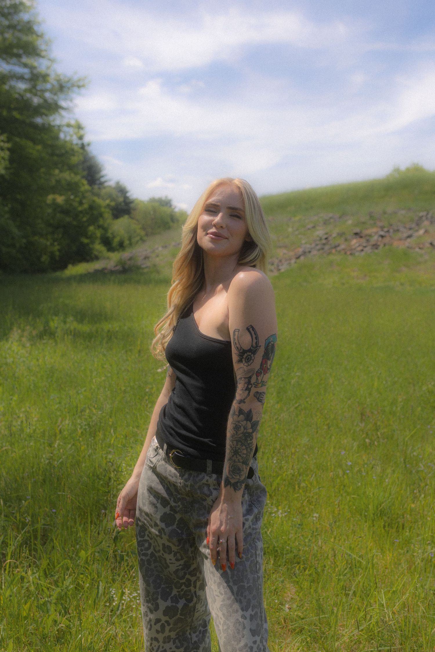 Candid shots in a summer field wearing a black tank top against a blue sky background.