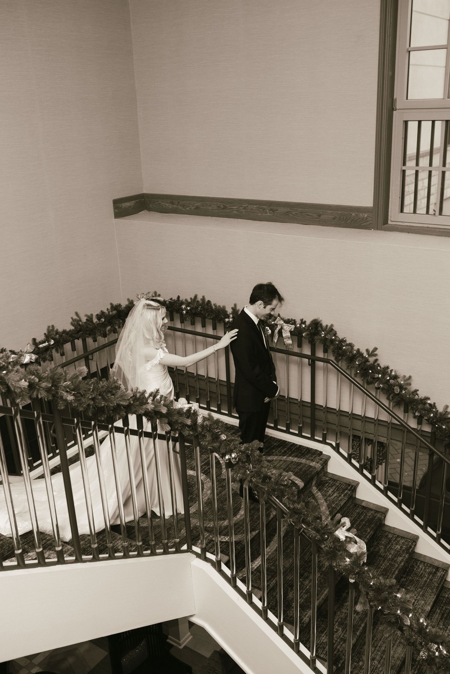 Black and white photo of wedding party descending an elegant staircase decorated with greenery.