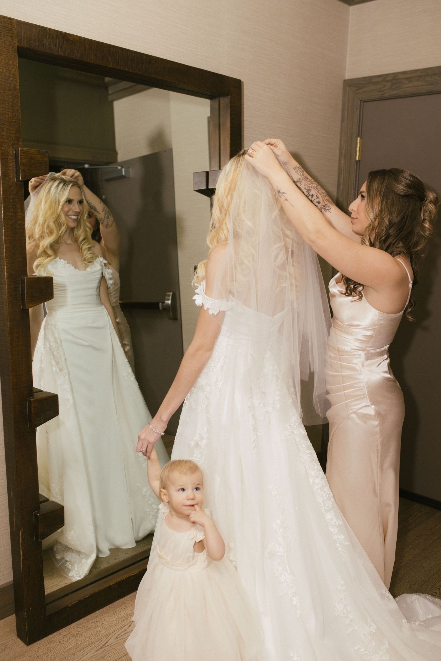 Getting ready scene with bridesmaids in blush dresses helping with wedding preparations.