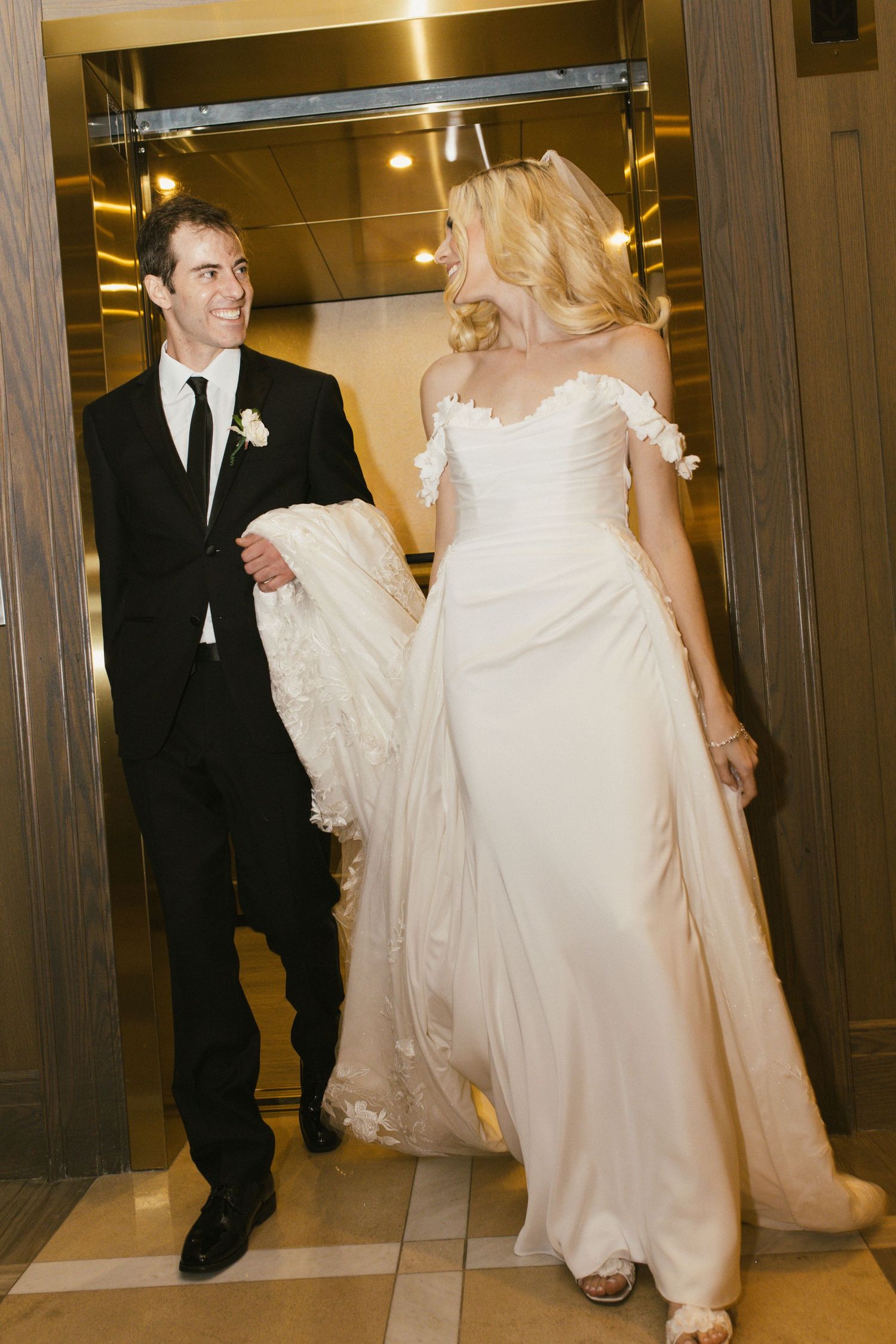 Candid moment of couple exiting elevator in wedding attire.