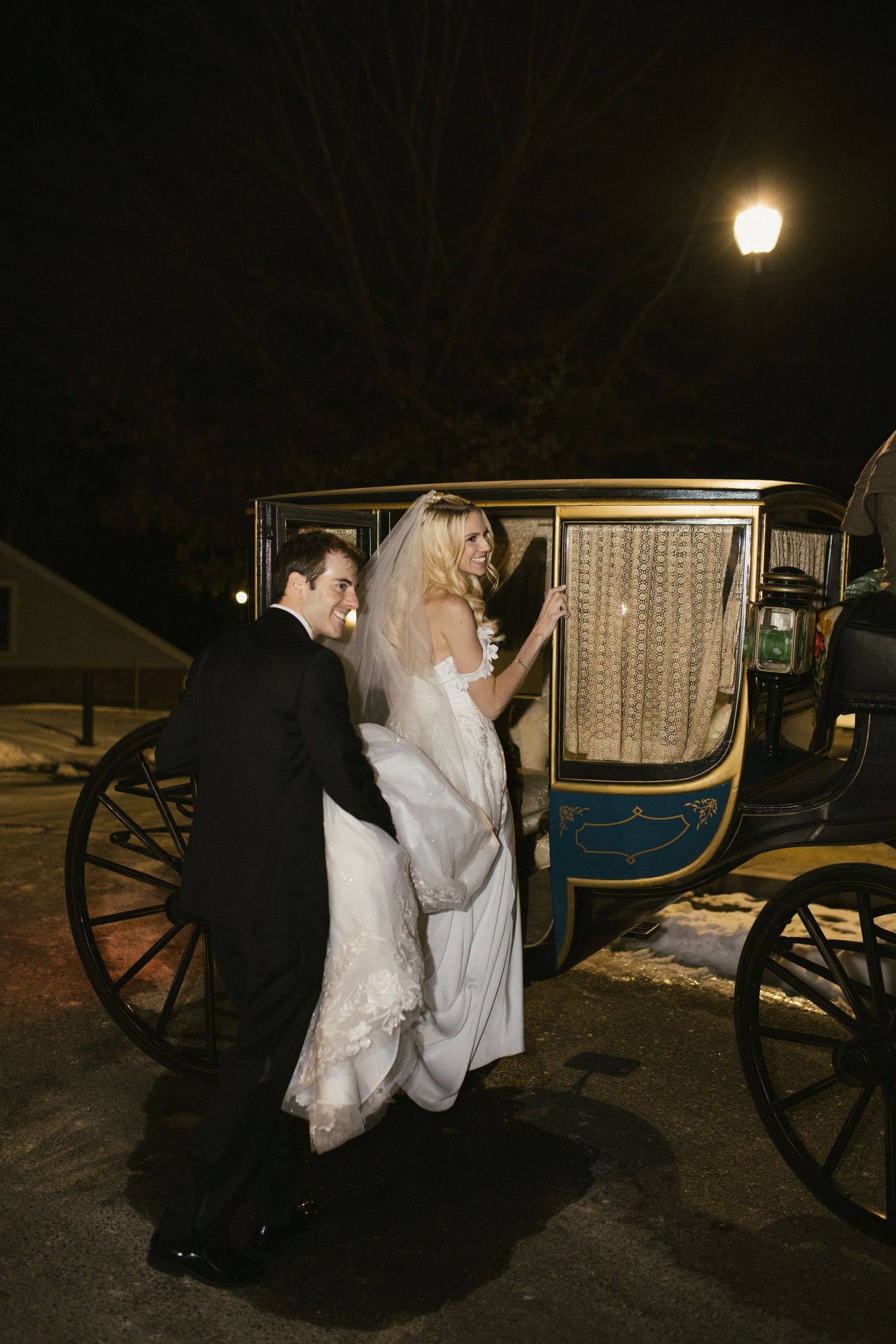 Wedding couple entering vintage horse-drawn carriage at night.