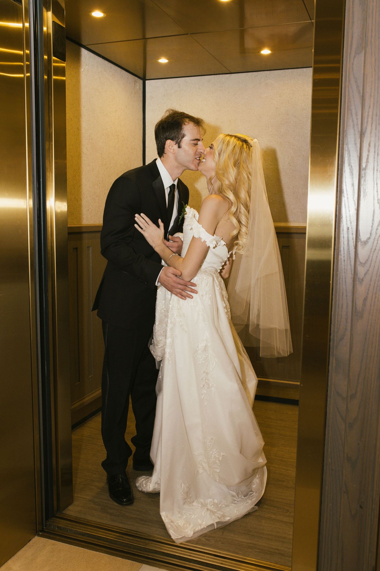 A romantic wedding couple sharing intimate moments in an elevator with mirrored walls.