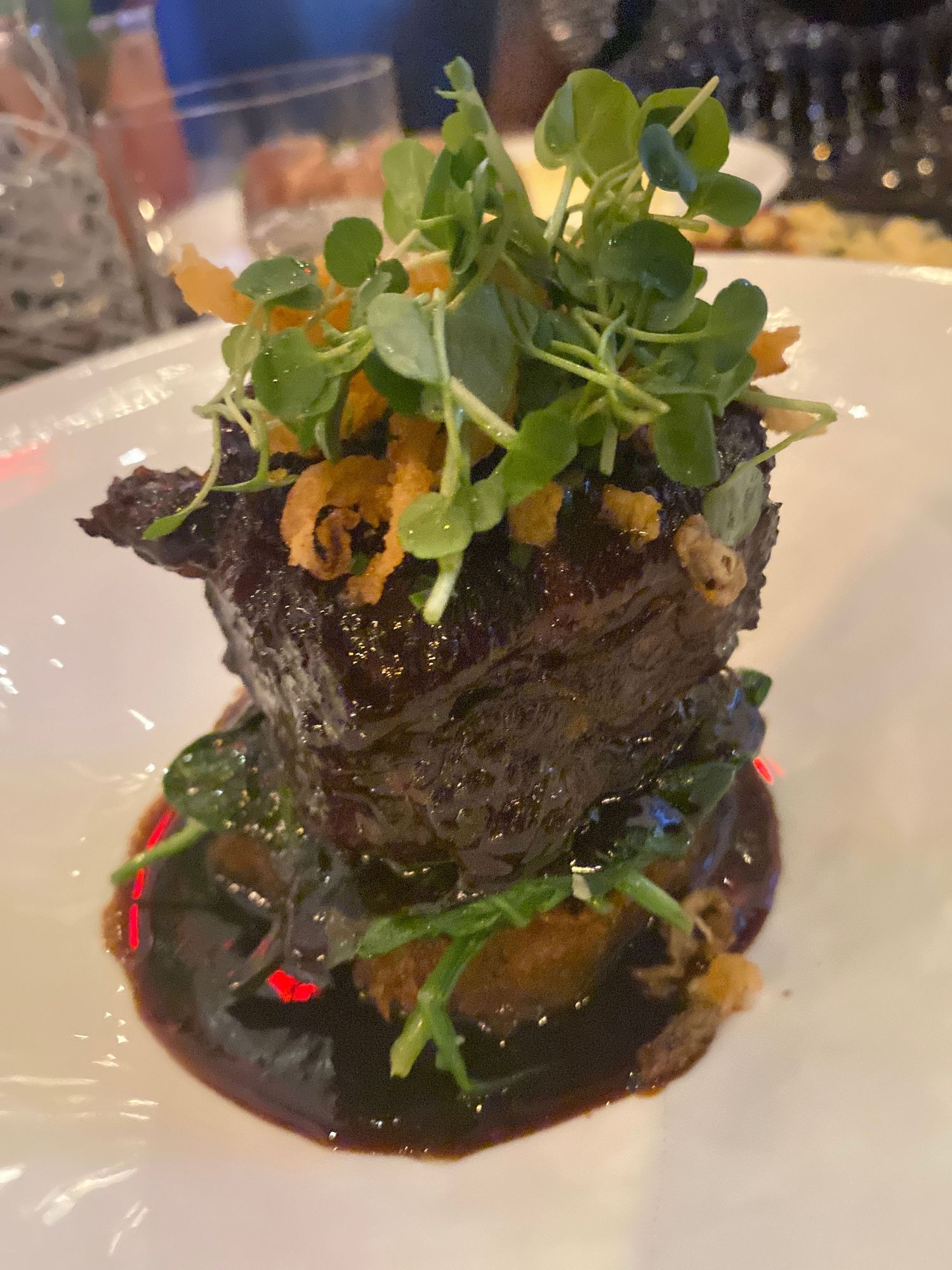 Braised beef short rib garnished with microgreens in a rich dark sauce.