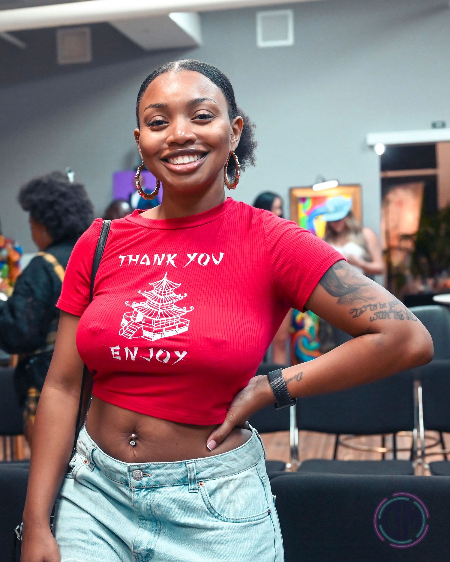 Person wearing red crop top with text and denim shorts poses showing tattoo.