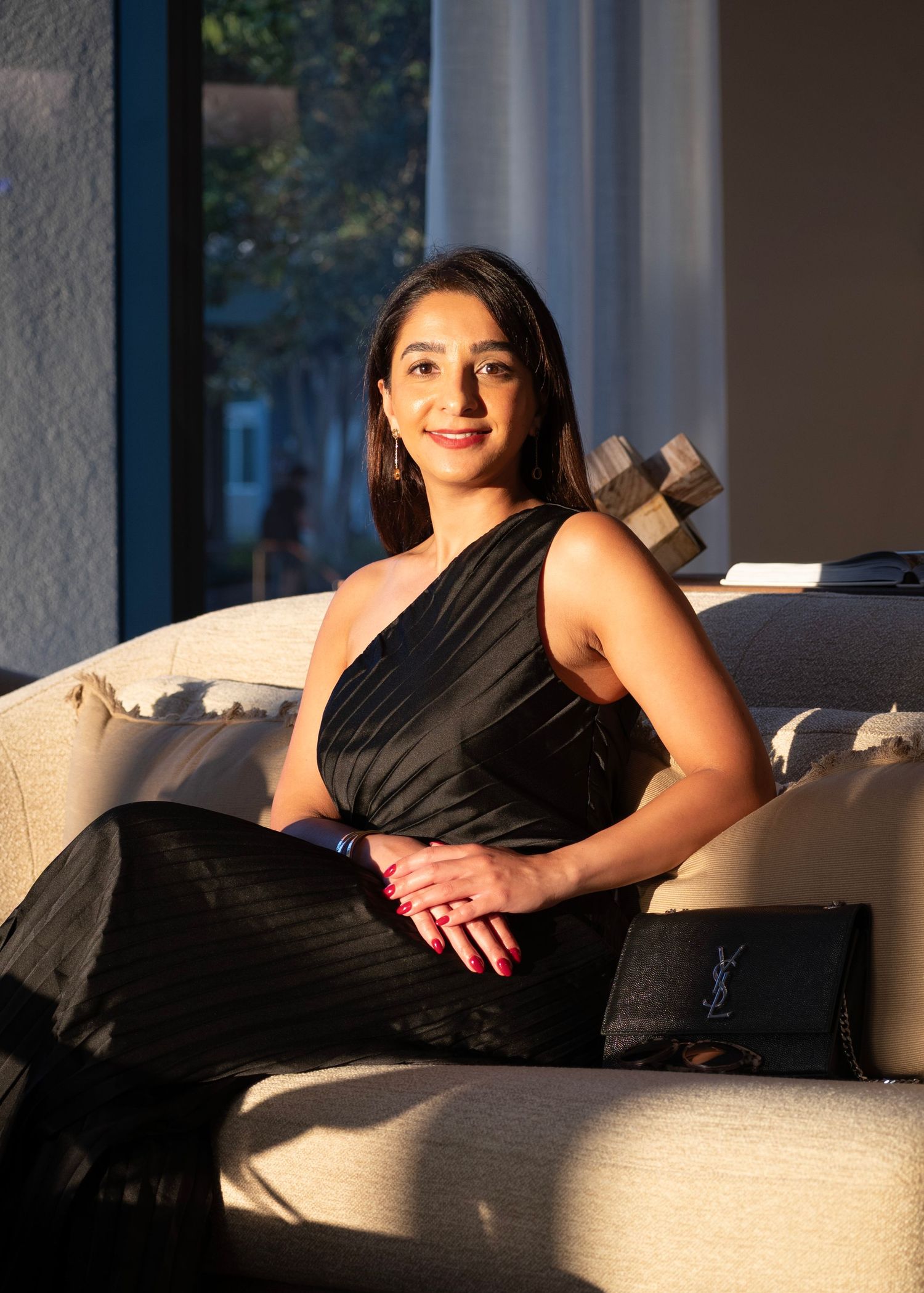 Woman in black dress lounging on white couch in elegant indoor setting.