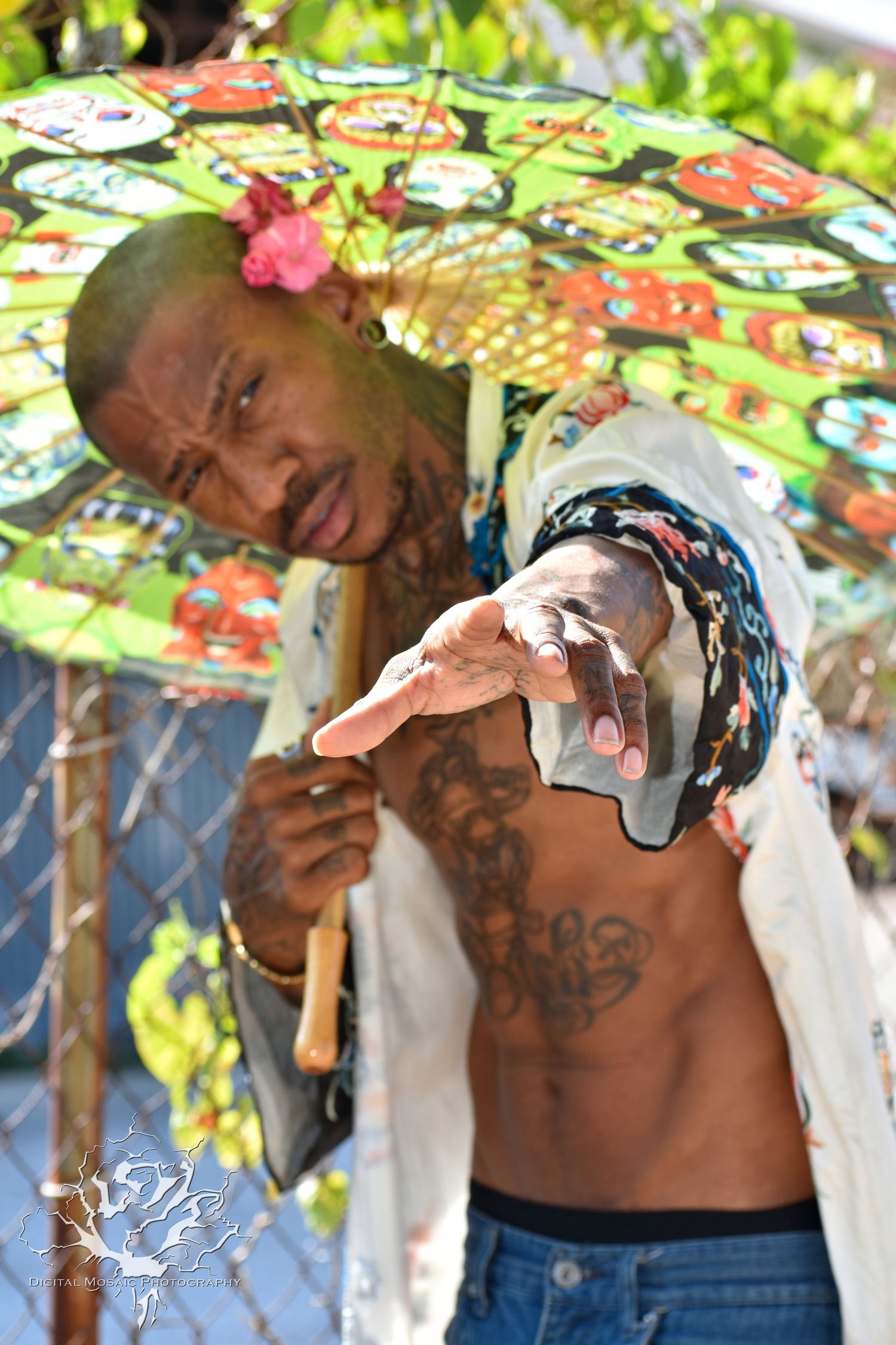 Artistic portrait under colorful umbrella with expressive hand gestures and tattoos.