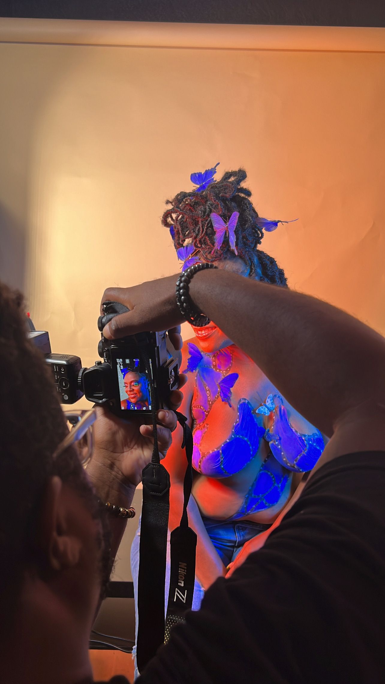 Behind the scenes photo showing camera setup with blue and pink lighting effects.